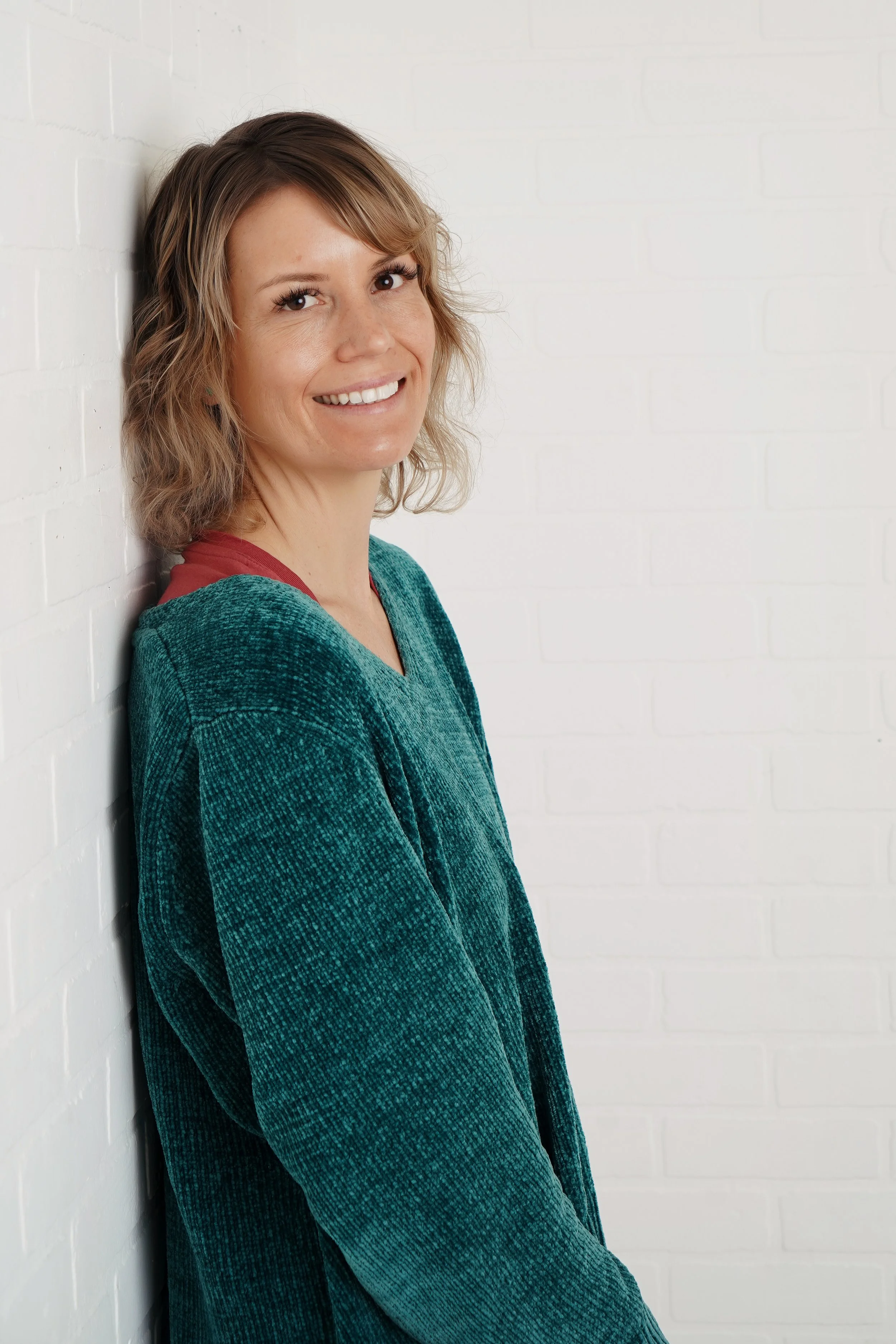 Jen Lescher smiling leaning against a white wall. If relationship OCD is affecting your life, a therapist can help. Reach out today for OCD counseling in Boston, MA.