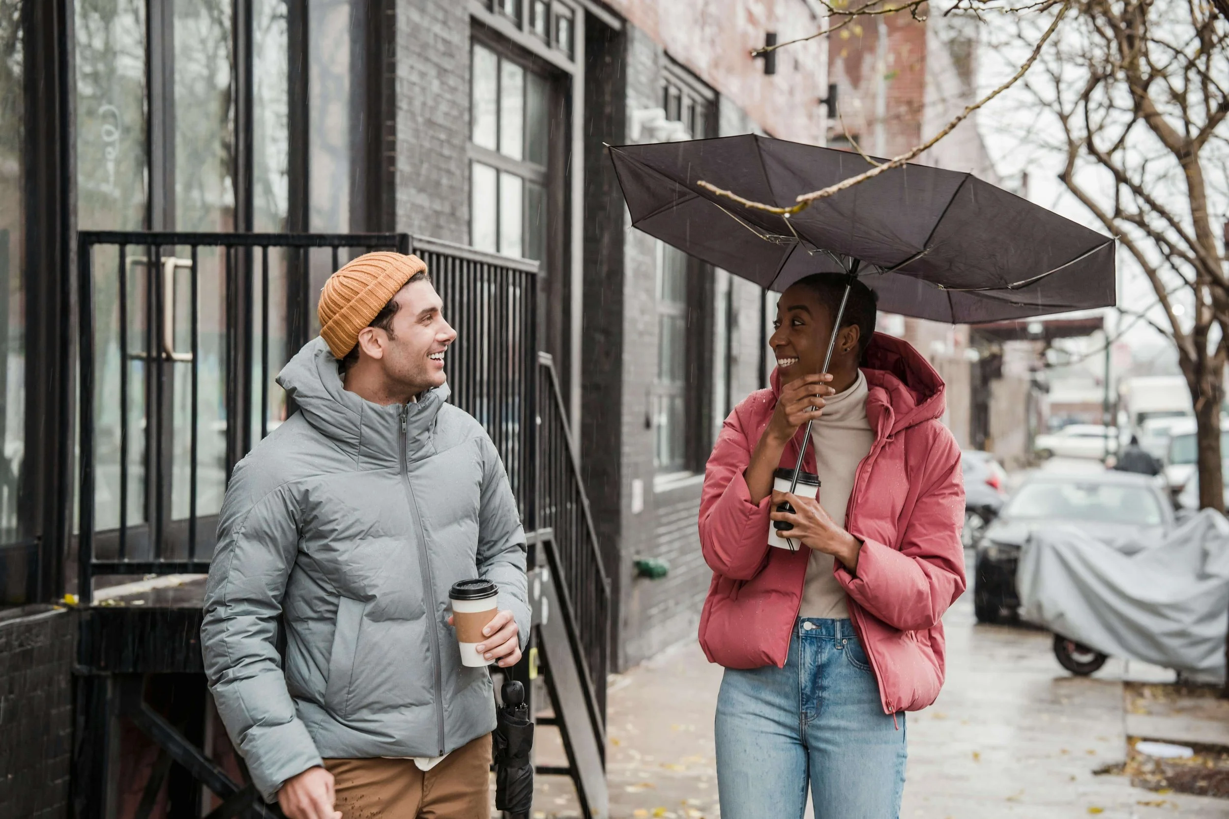 2 diverse friends walking down the street with an umbrella holding coffee. If you want to learn how to manage your OCD, I'm here to help. I offer therapy for OCD & anxiety in Boston, MA for individuals struggling with overthinking. Learn more here!