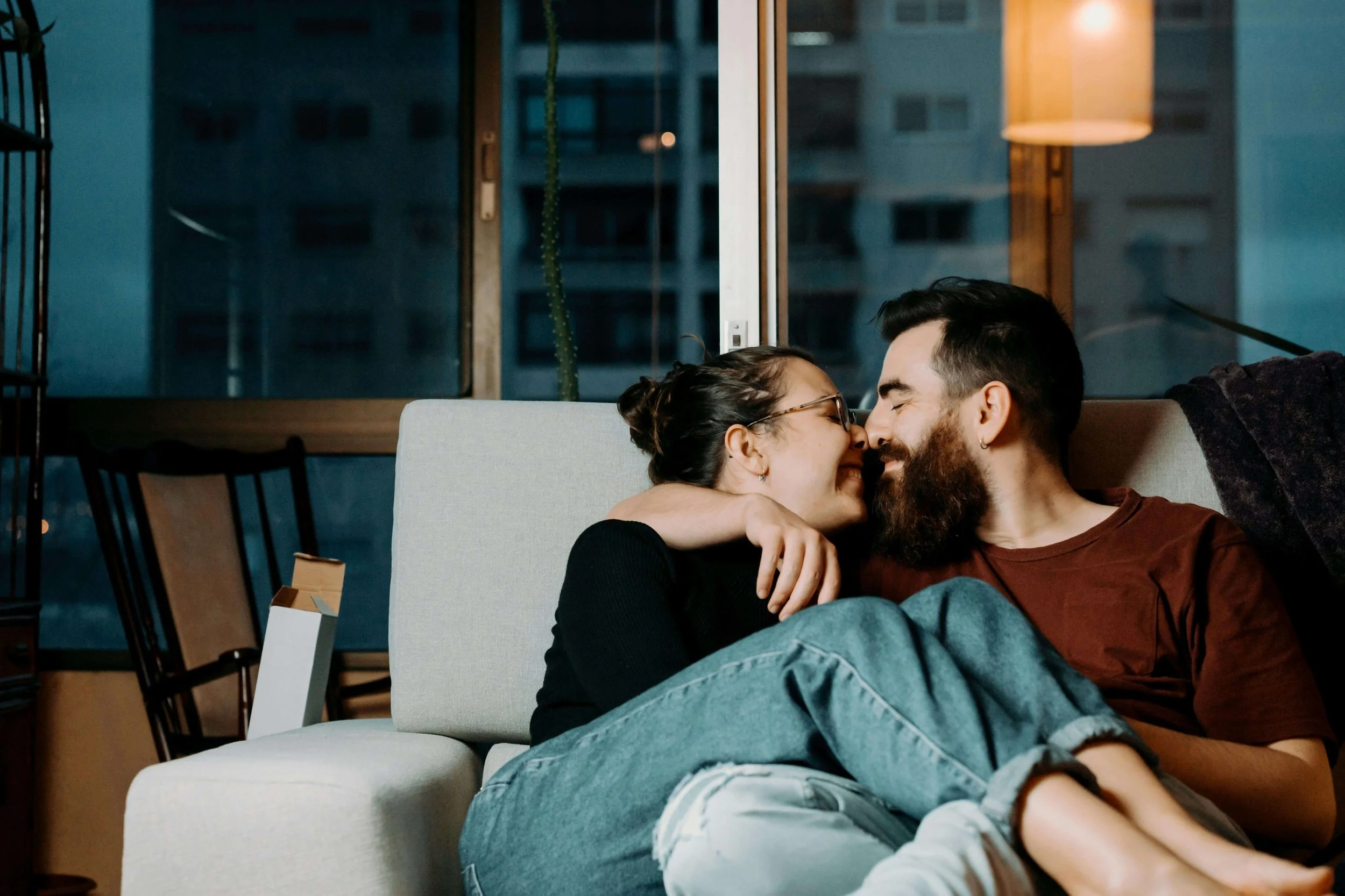 A couple sitting close together on the couch touching each other's noses. ERP therapy in Boston, MA is here to support you with relationship OCD & uncertainty. Get started today.