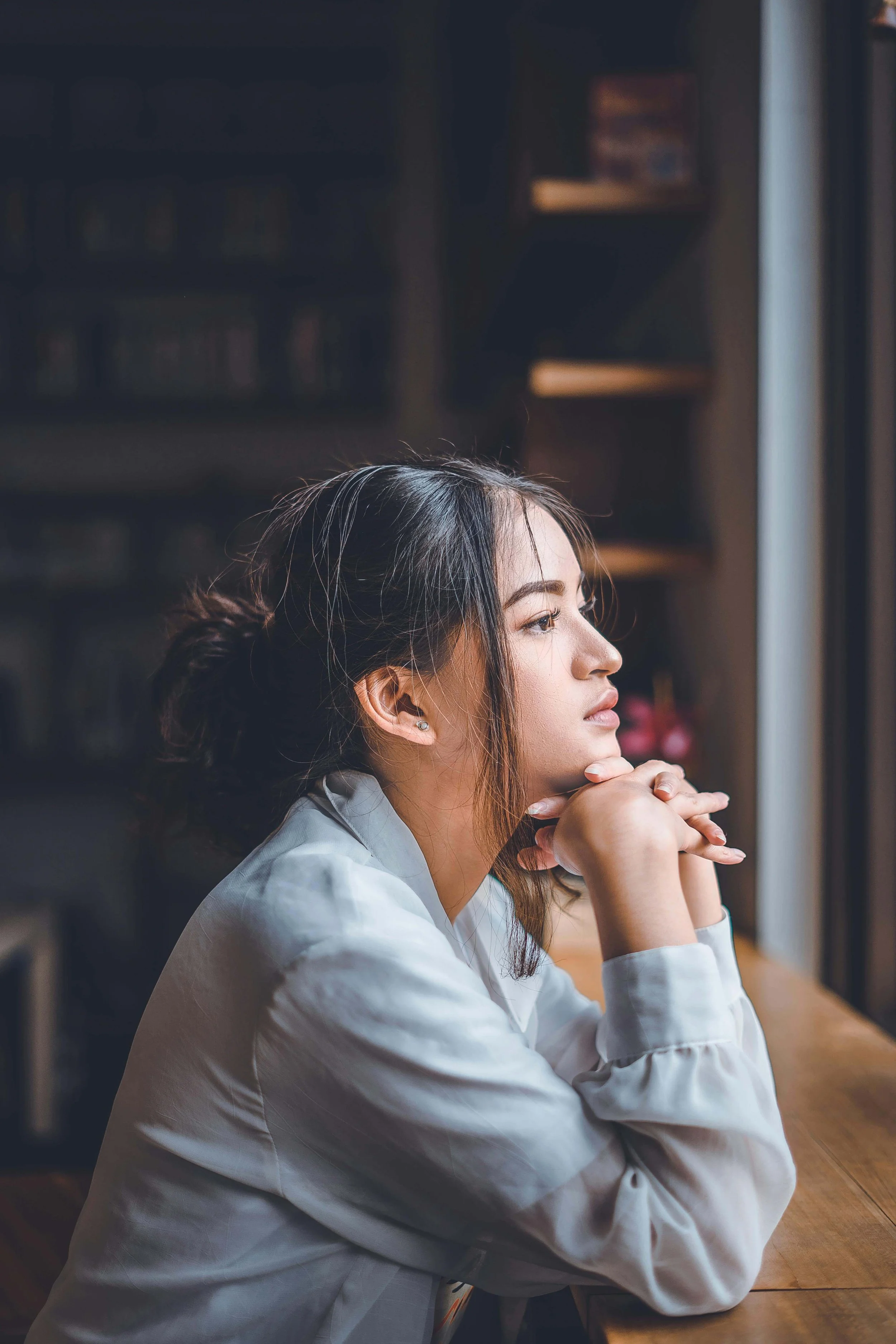 An anxious woman sitting at a table looking out the window. representing how anxiety & OCD can affect your relationships with ruminating, overthinking and doubt. Explore how ERP therapy in Boston, MA can help.