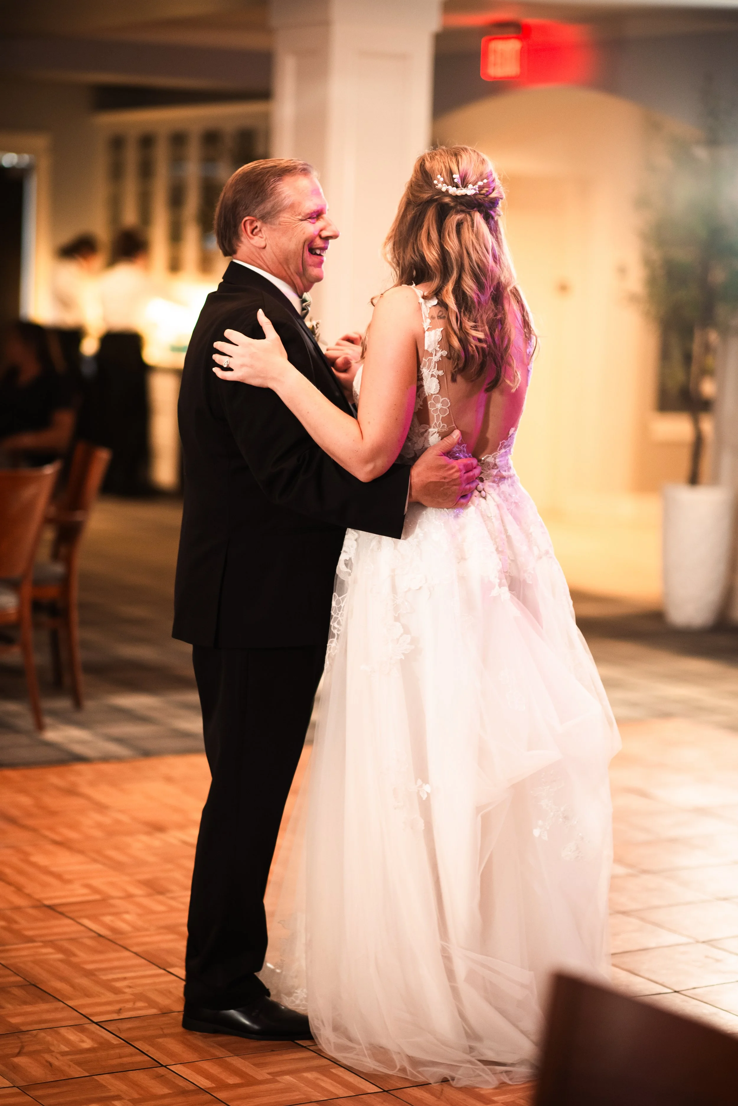 A bride and an older man, possibly her father, dancing and smiling at a wedding reception.