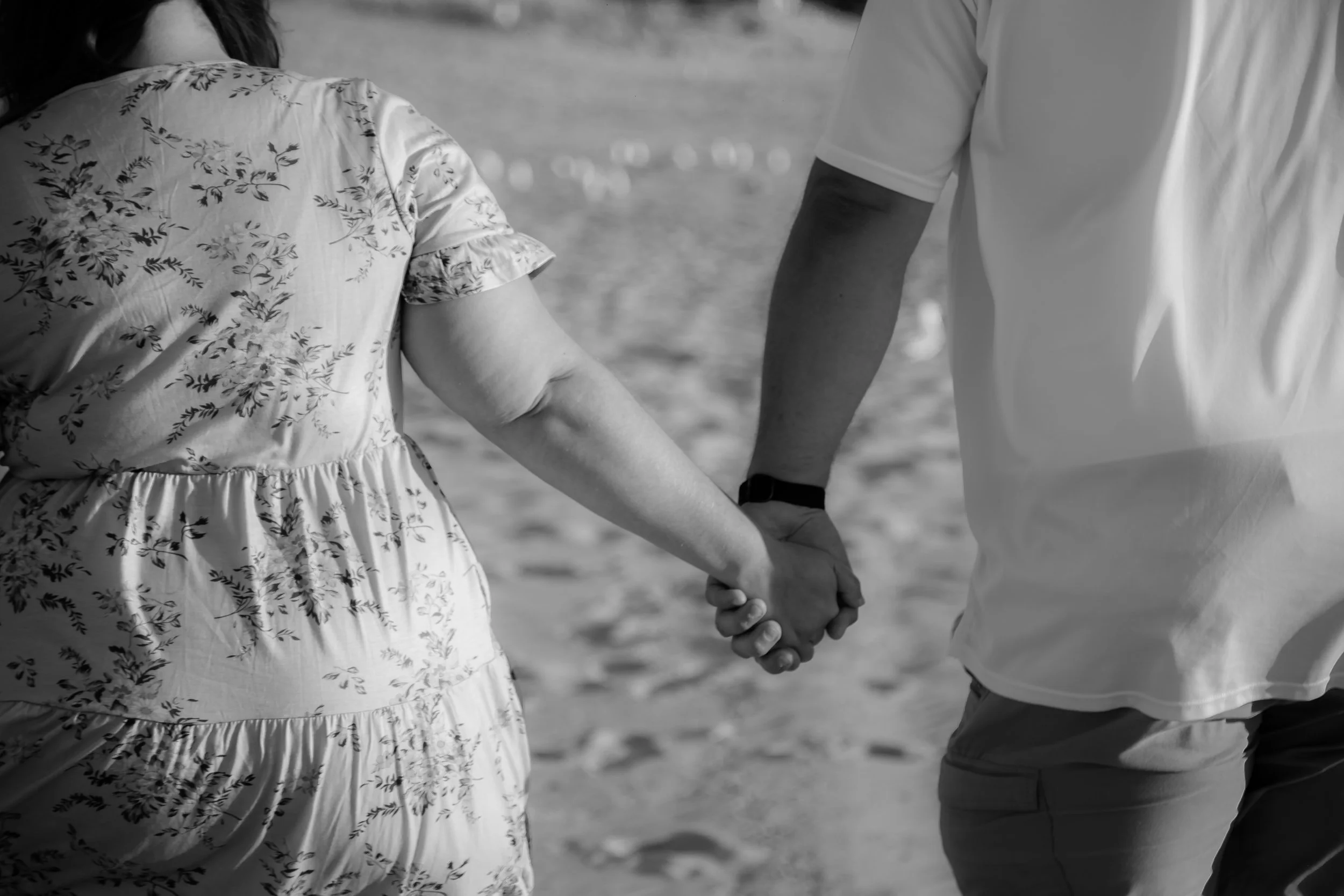 A couple holding hands while walking on a beach.