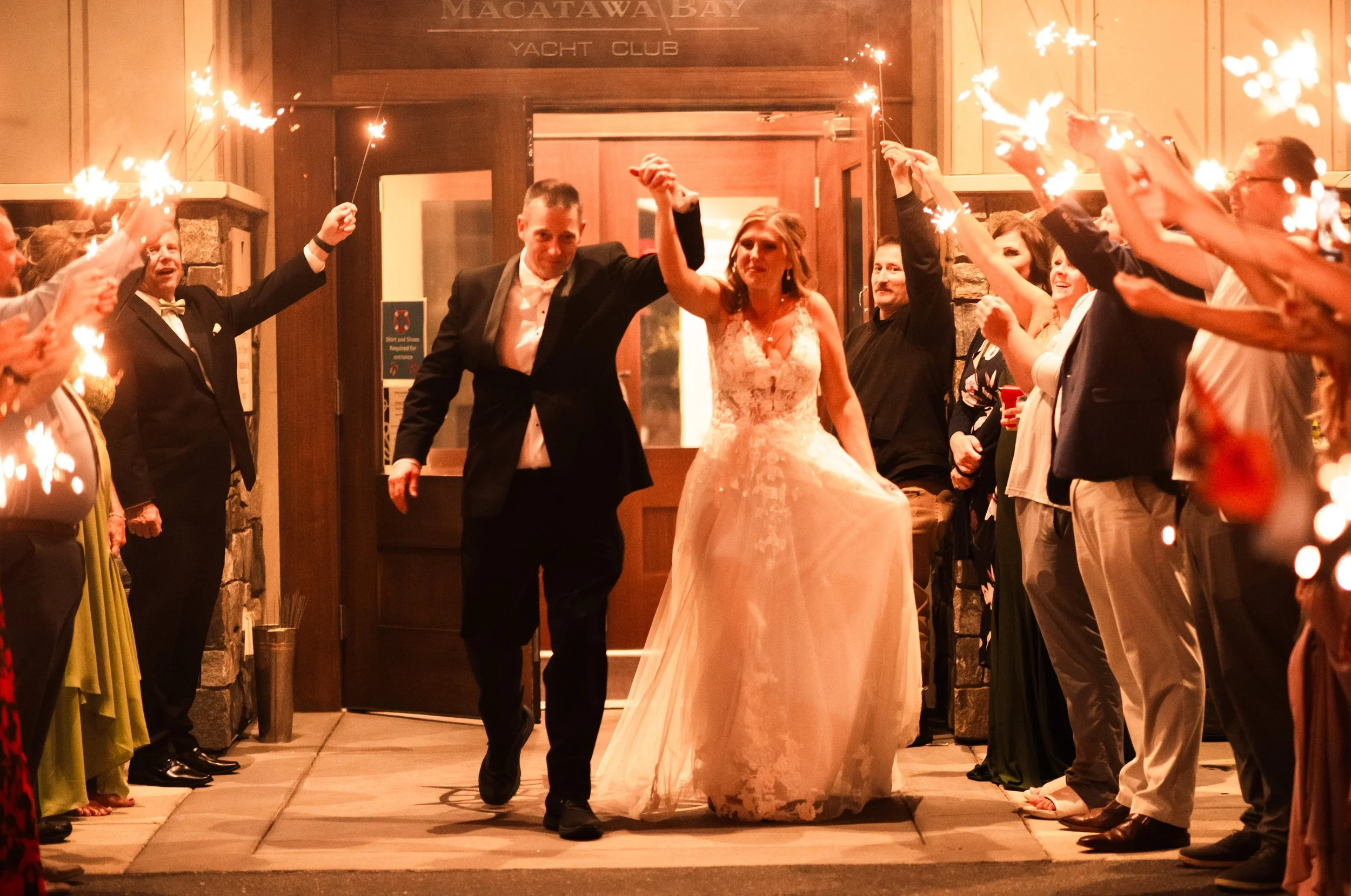 A newlywed couple is walking arm in arm through a tunnel of guests holding sparklers during a wedding celebration at night.
