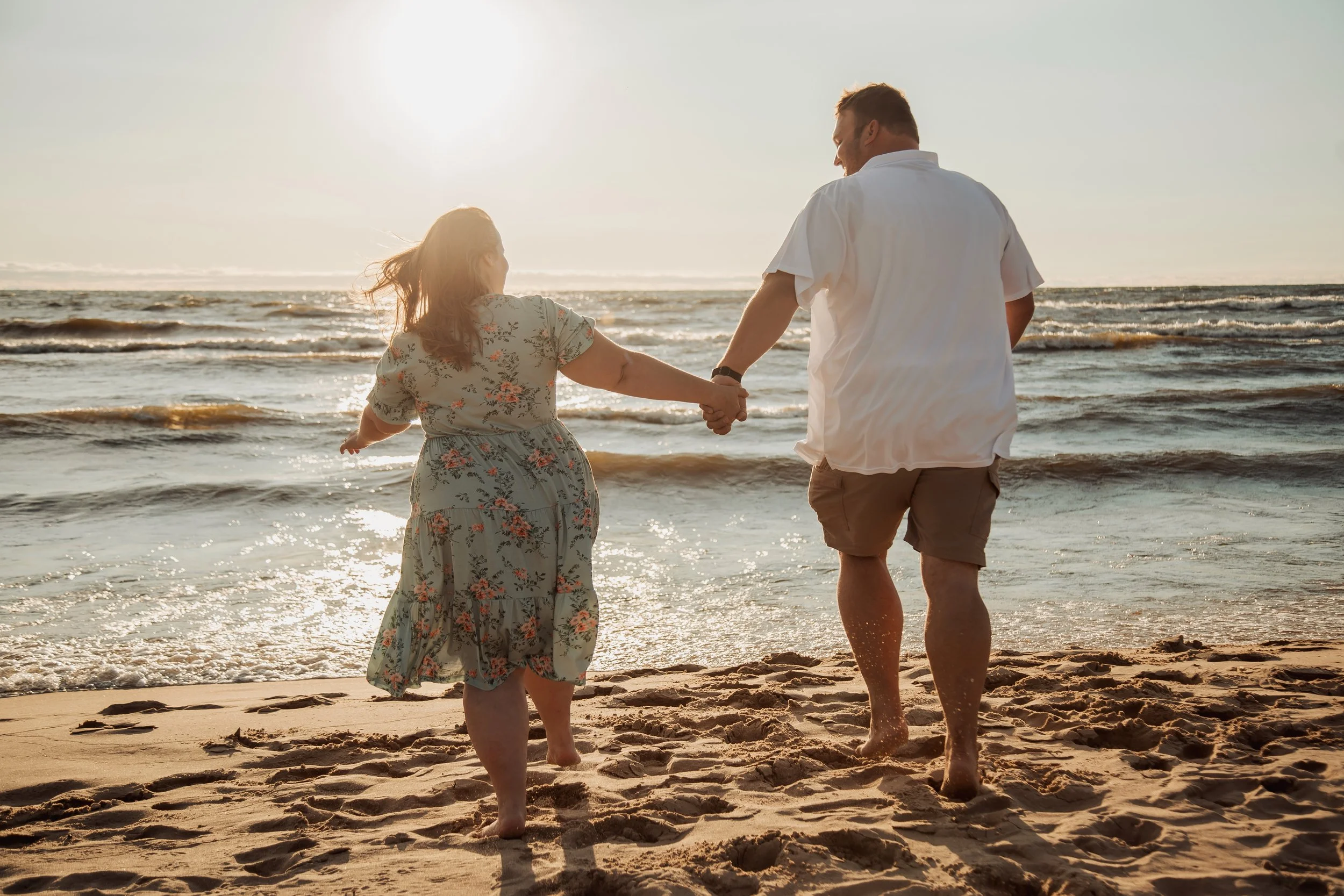 A couple holding hands walking on a beach at sunset.