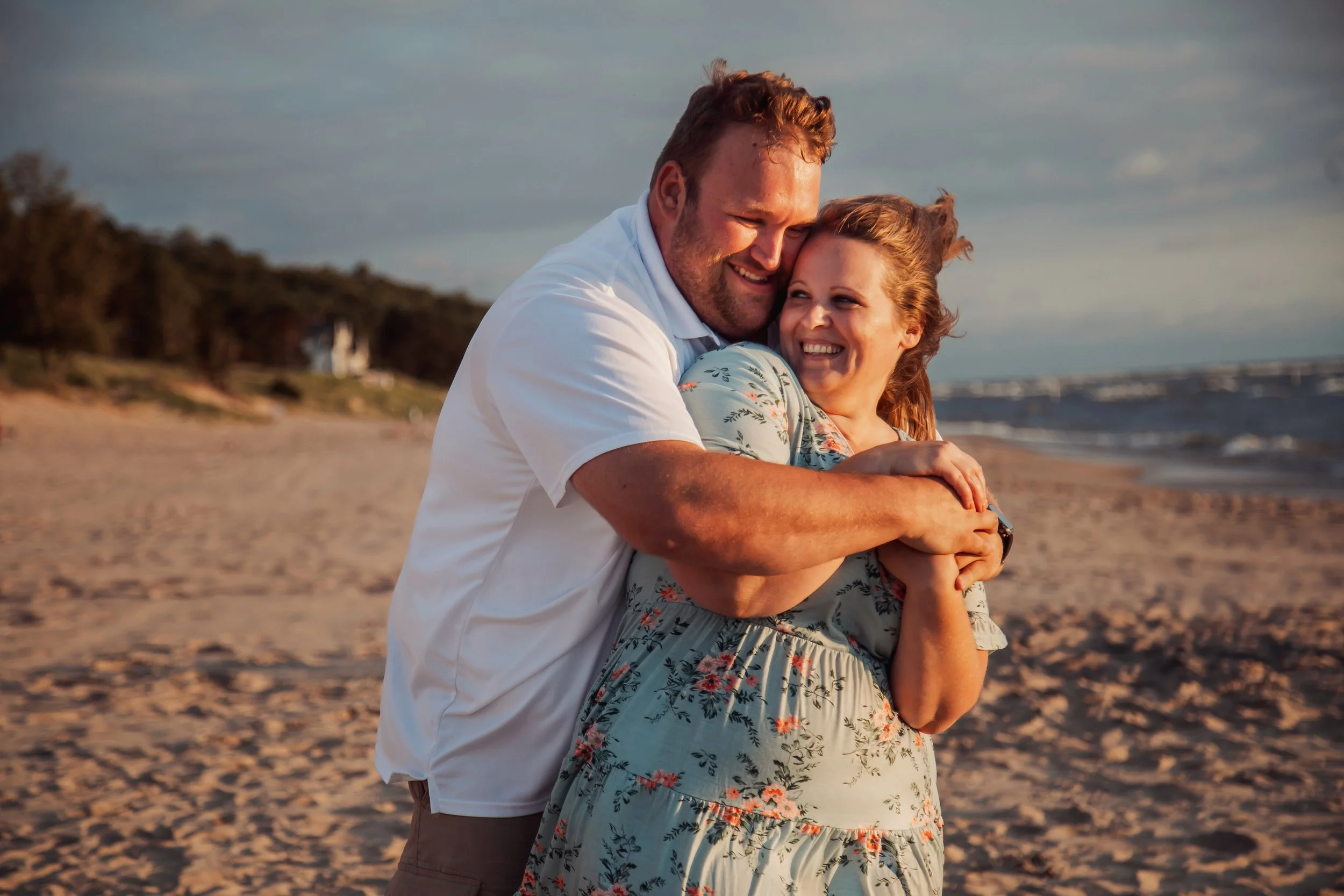 A happy couple hugging on a beach during sunset.