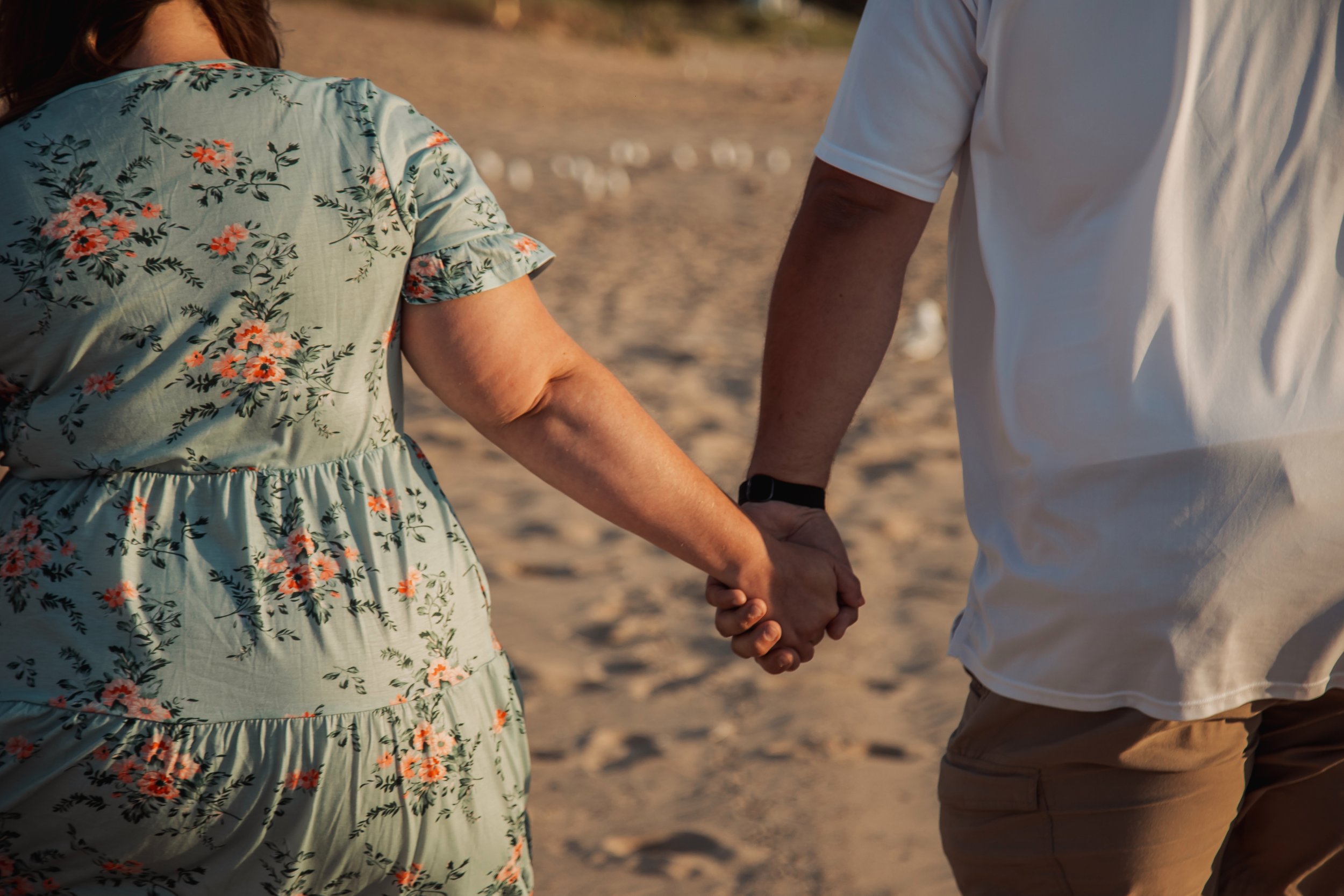 A man and woman holding hands while walking on the beach during sunset.