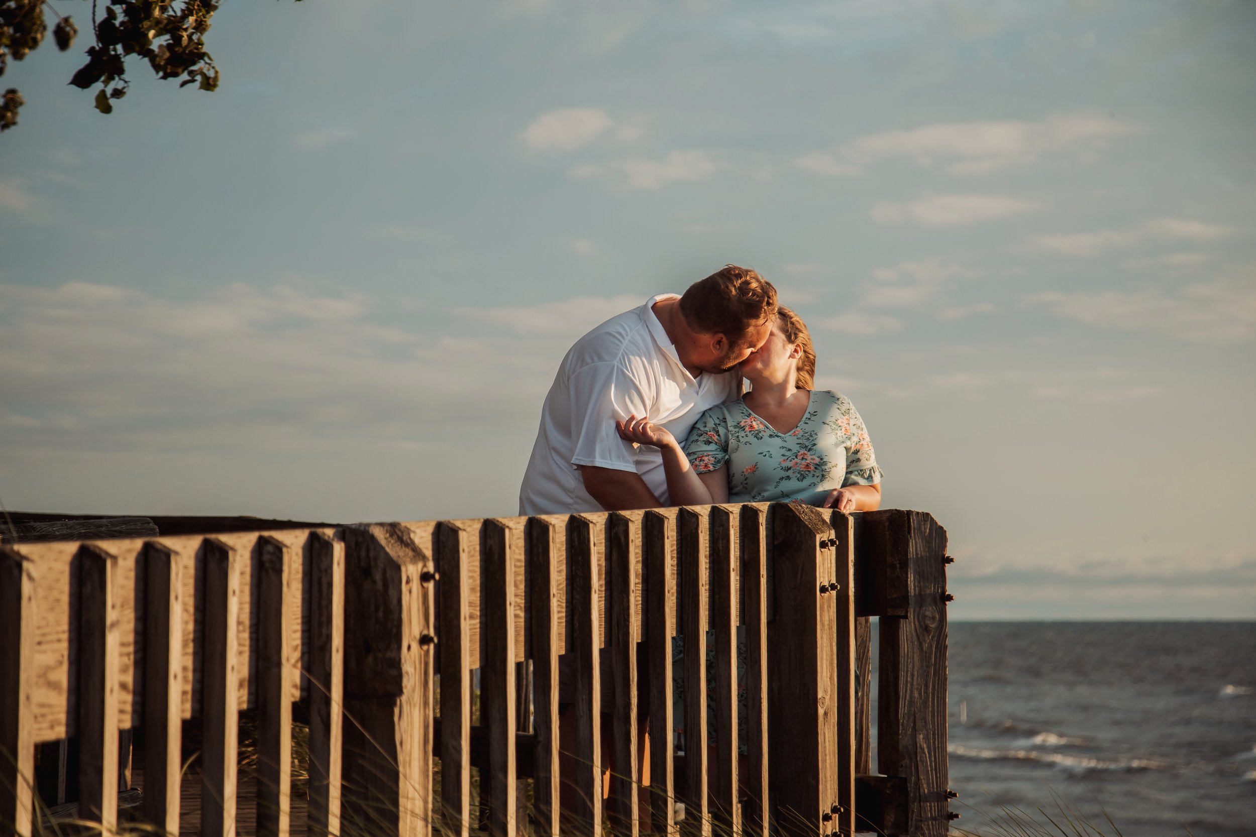 A couple sharing a kiss on a wooden pier by the water during sunset.