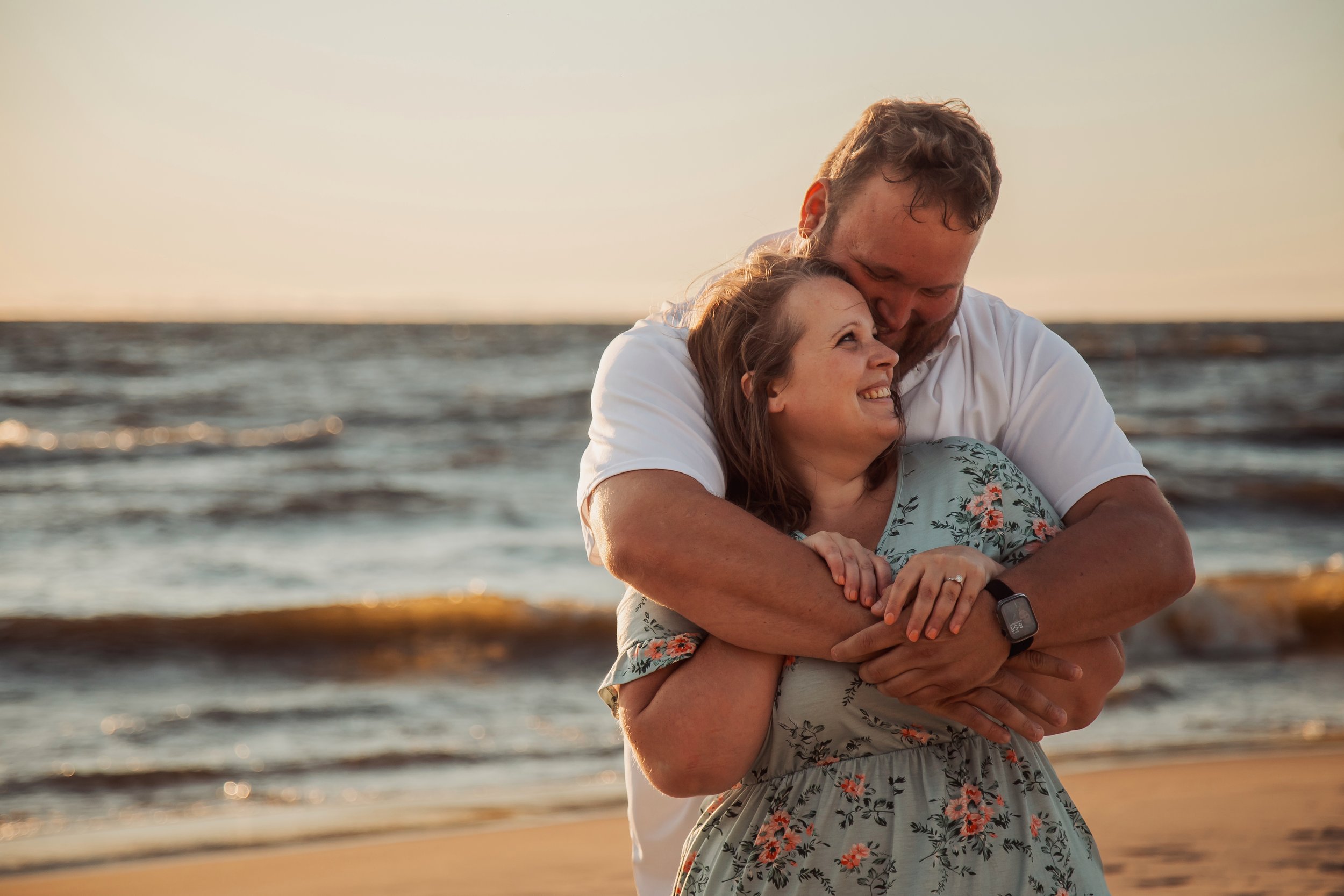 A couple hugging on the beach at sunset, with the ocean in the background.