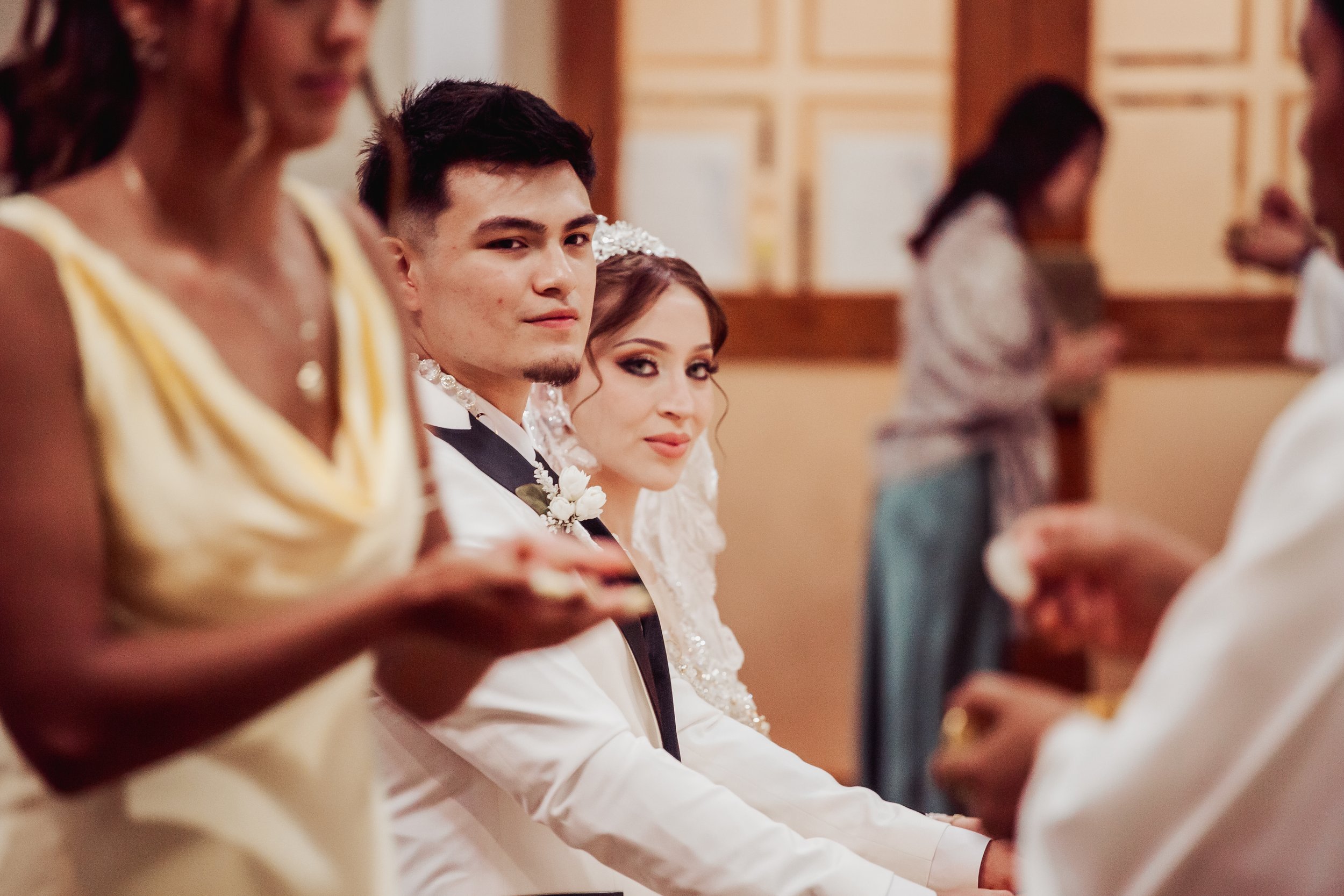 A wedding ceremony with a bride and groom holding hands, surrounded by wedding guests in a church or chapel.