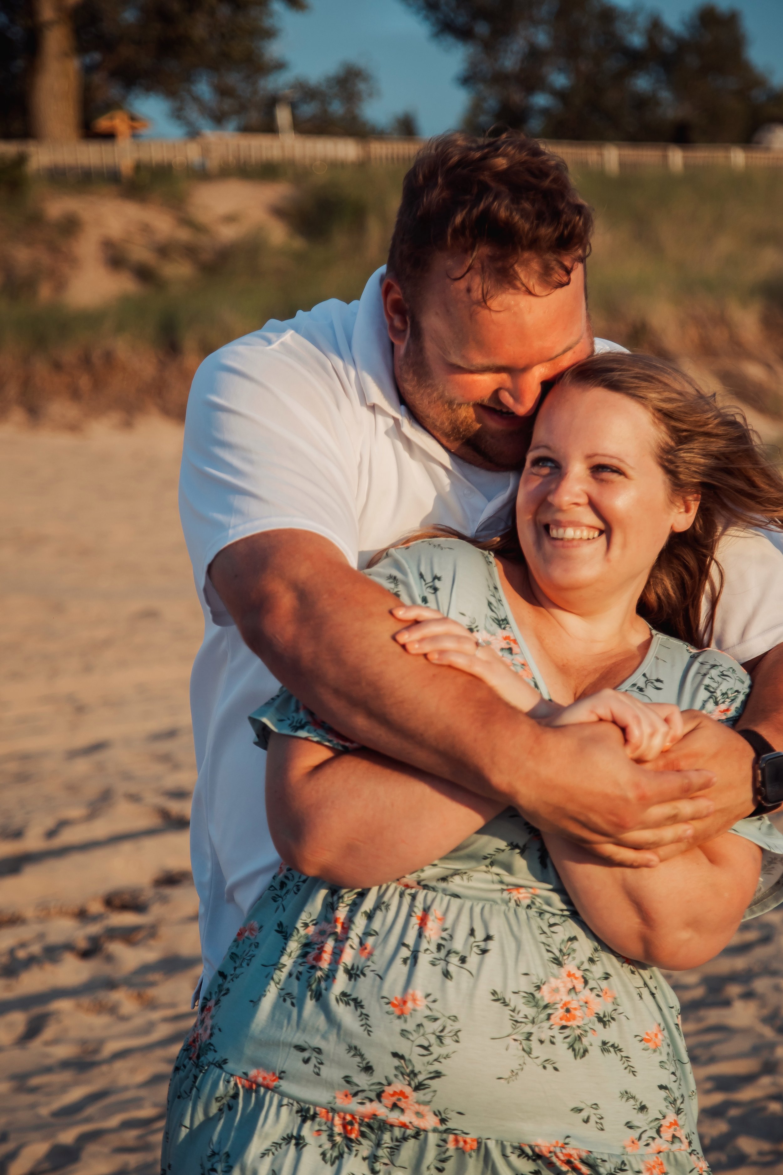 A happy couple on a beach, embracing and smiling at each other during sunset.