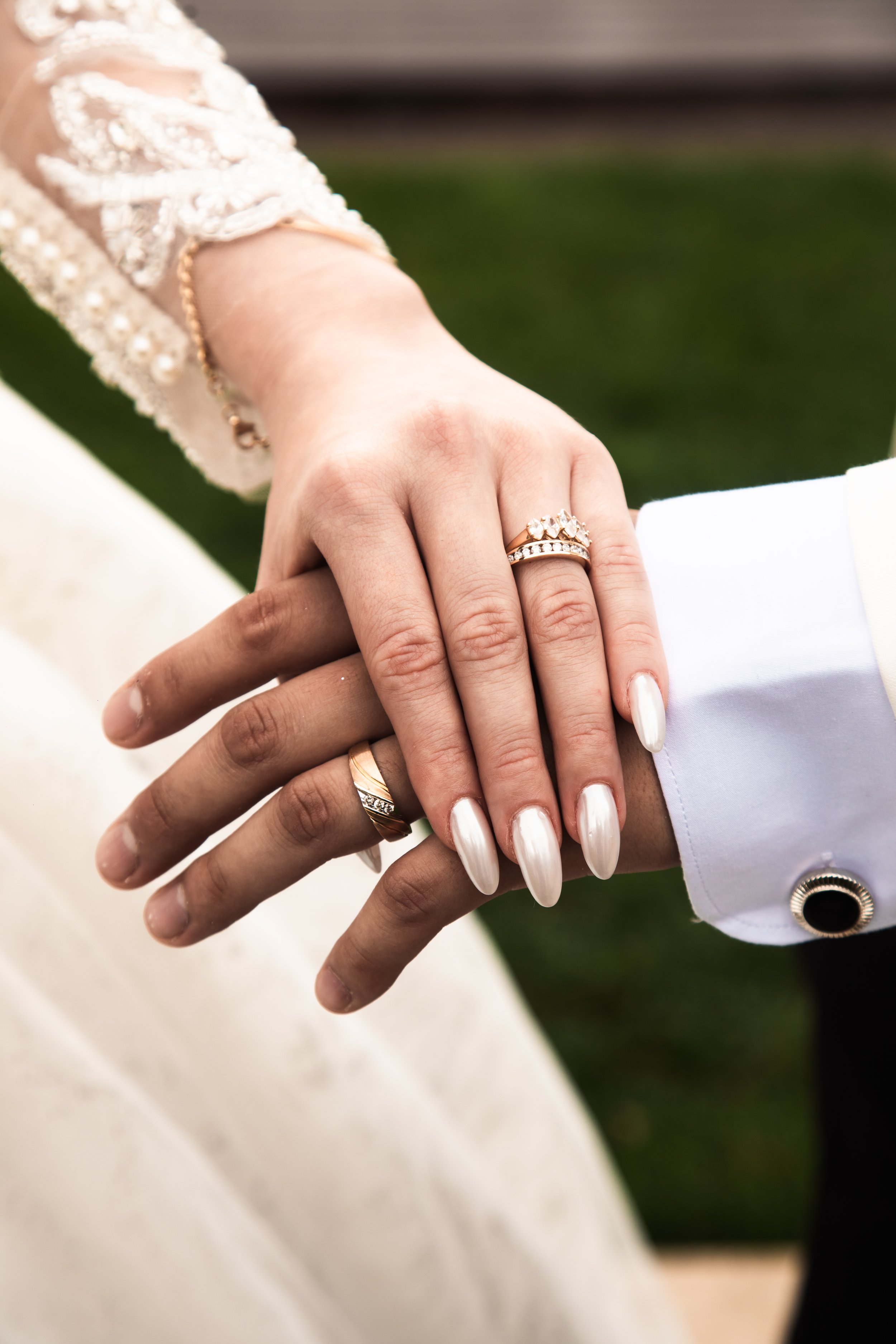 Close-up of a bride and groom's hands with wedding rings, holding each other gently.