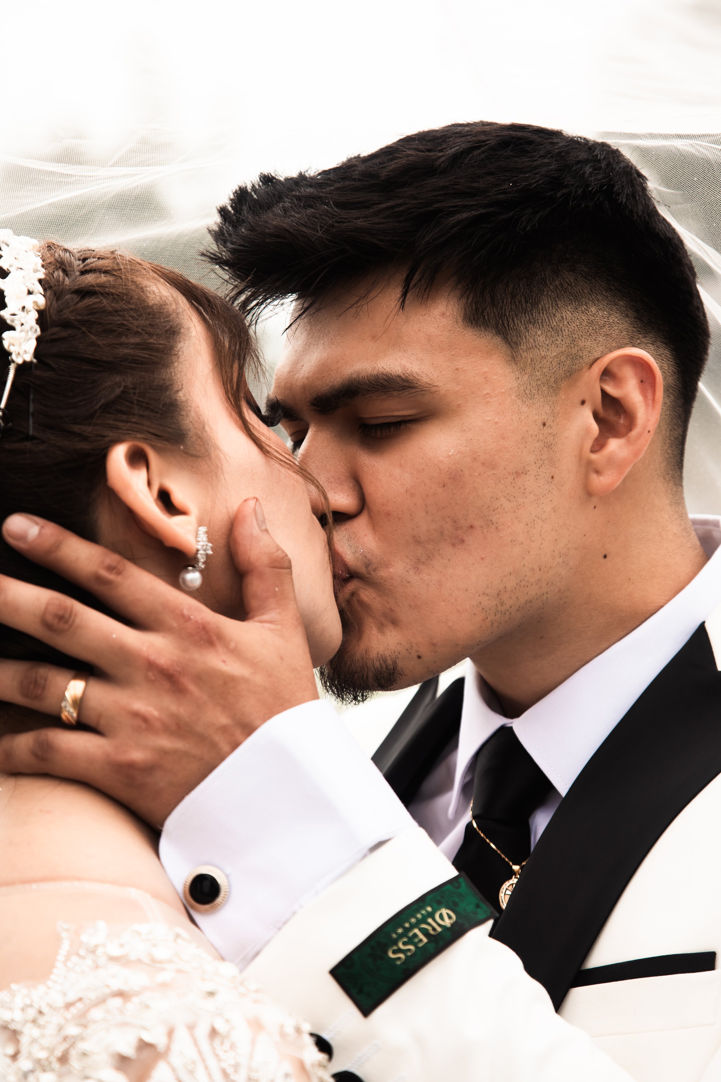 Close-up of a couple kissing on their wedding day, with the groom in a tuxedo and the bride in a wedding gown with jewelry.