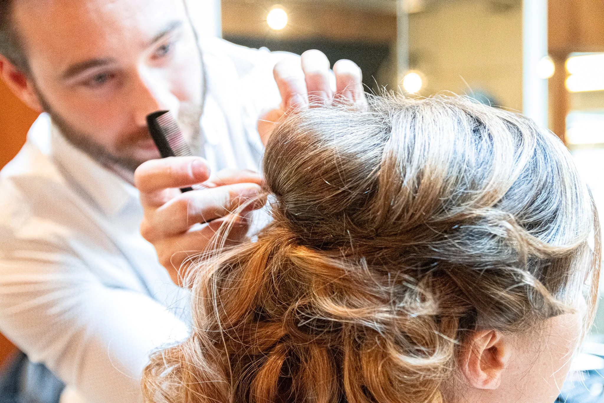 A hairstylist uses scissors and a comb to style a woman's hair in a salon.