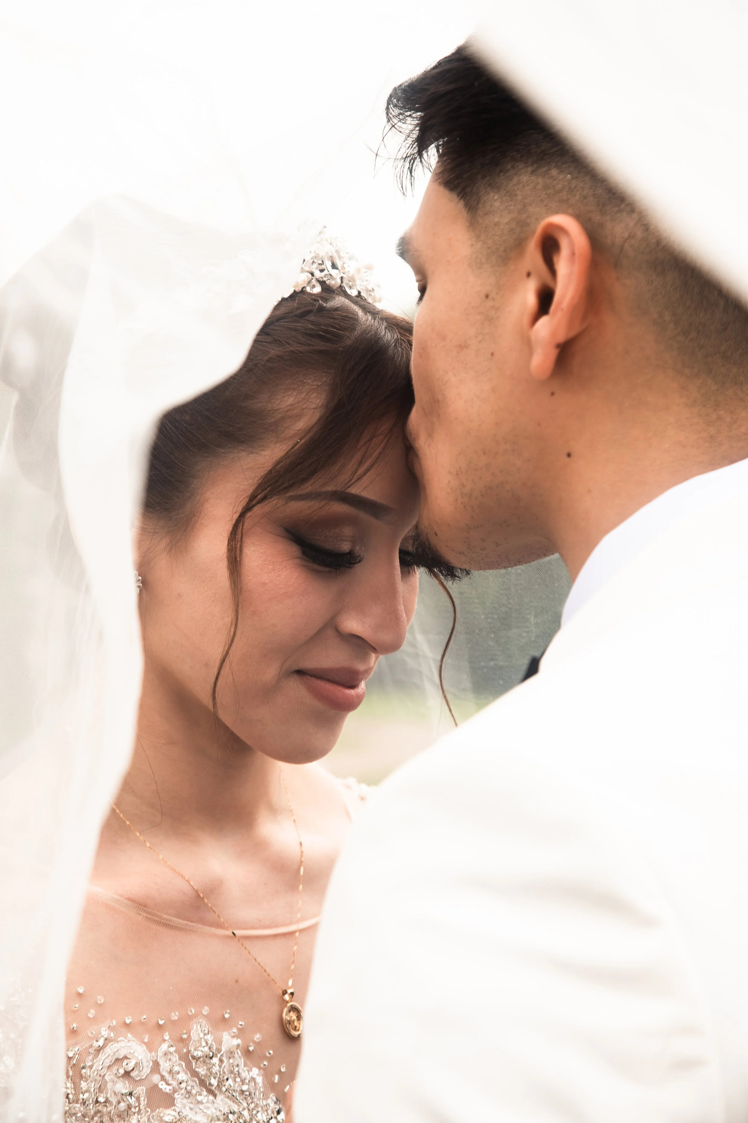 A bride and groom sharing an intimate moment, with their foreheads touching and eyes closed, under the bride's veil.