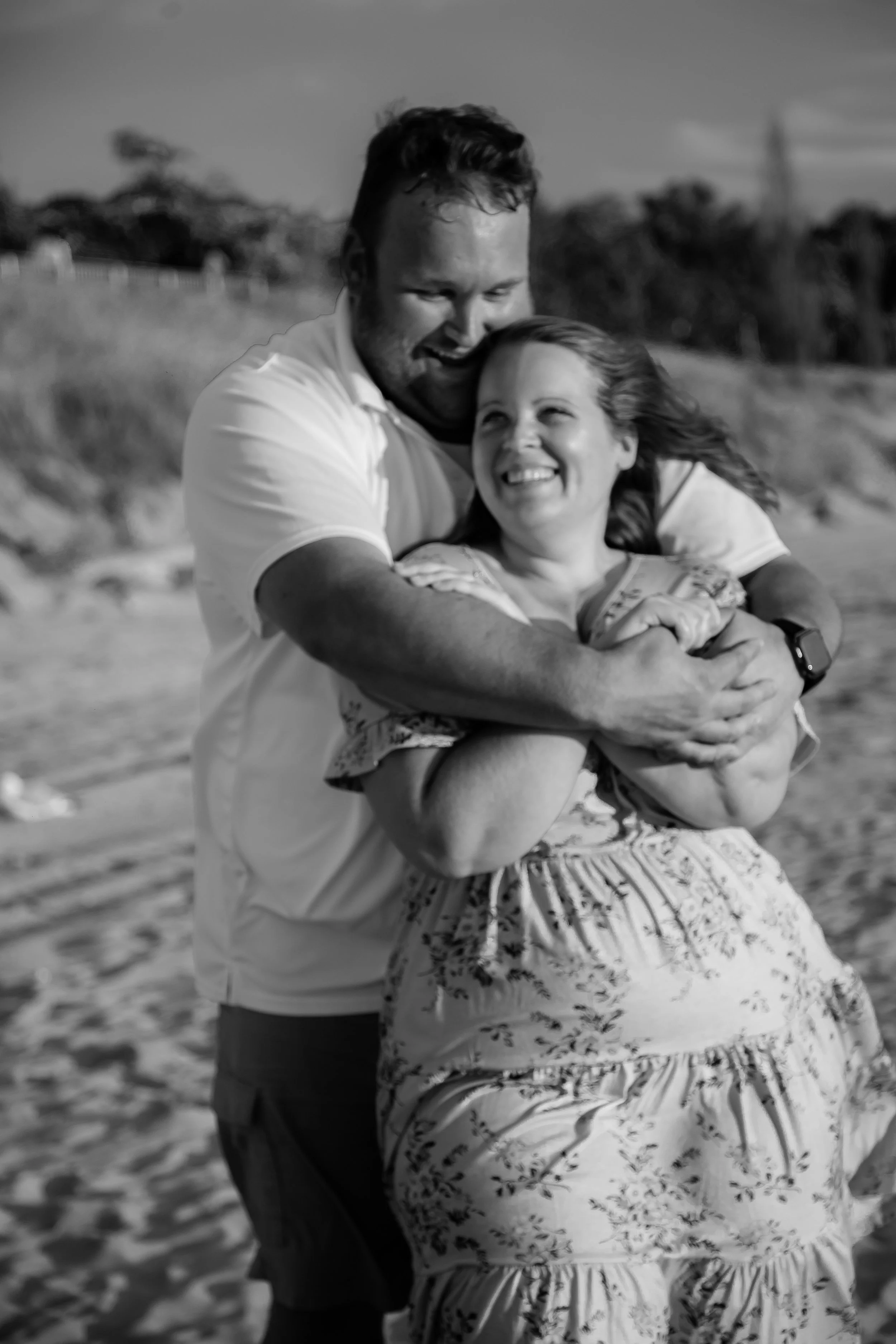A man and a woman smiling and hugging on the beach.