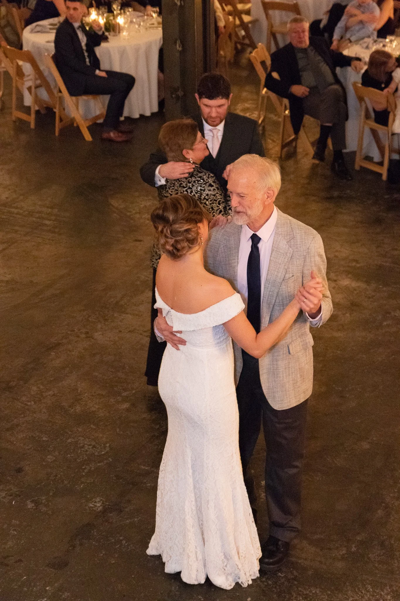 Couple dancing at a wedding reception surrounded by seated guests and candlelit tables.