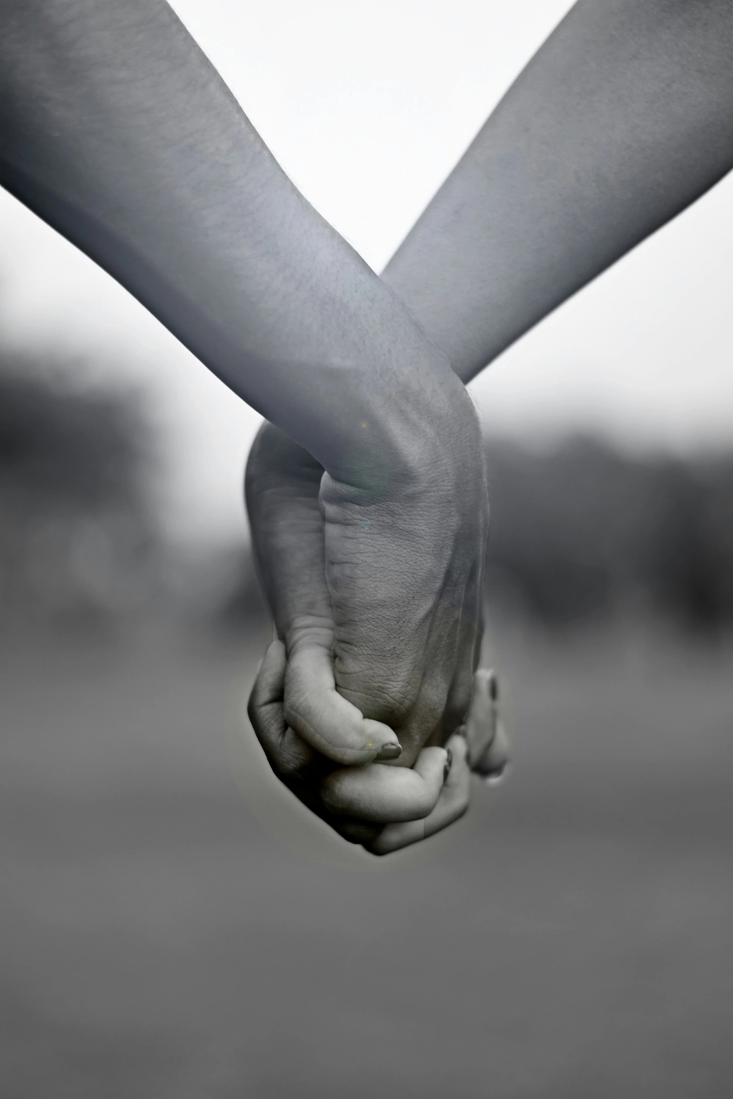 Black and white photo of two people holding hands with fingers intertwined.