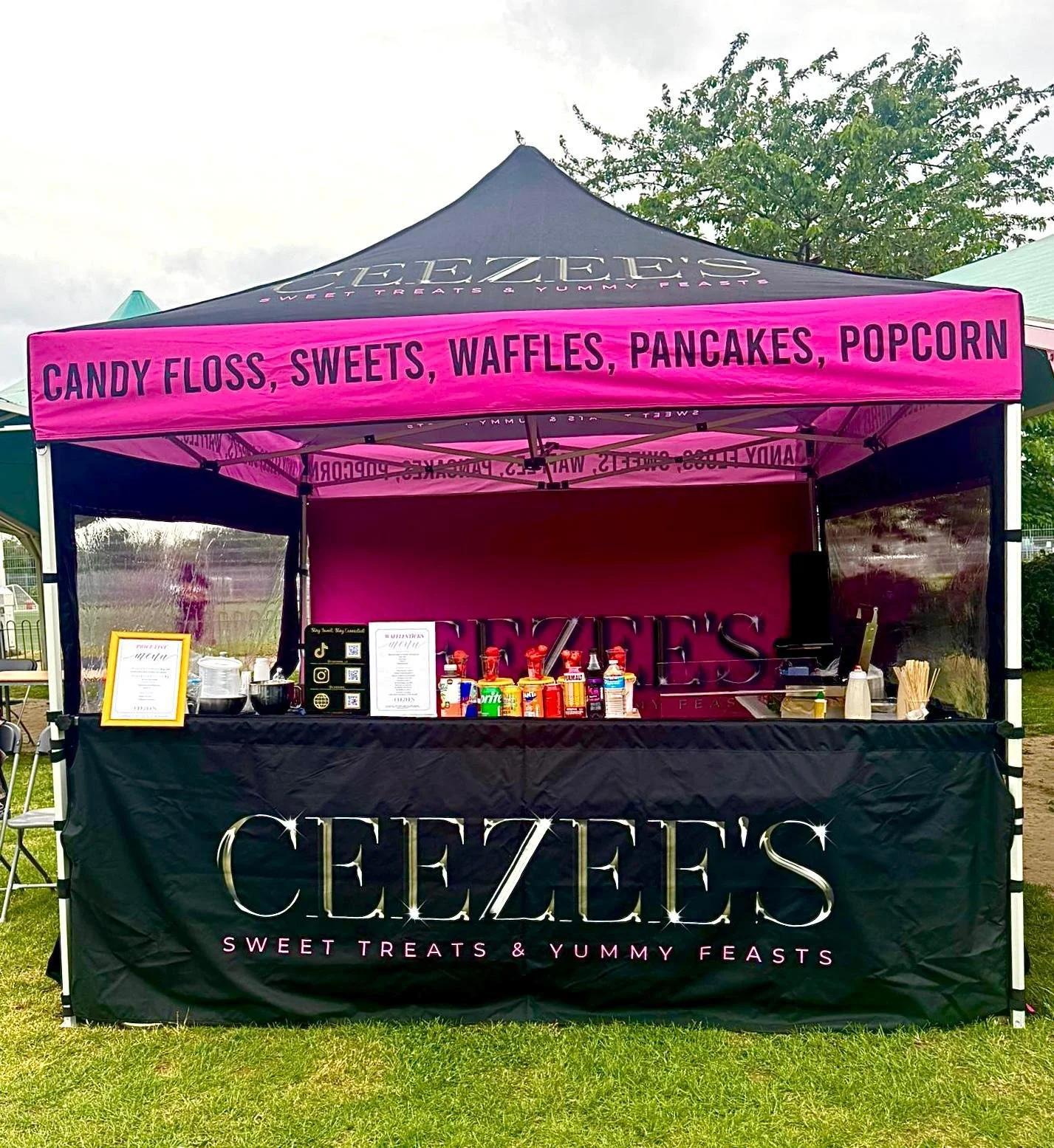 A pink and black tent at an outdoor fair for Ceezies, a sweets and treats stand, with candy, popcorn, and snacks on display.