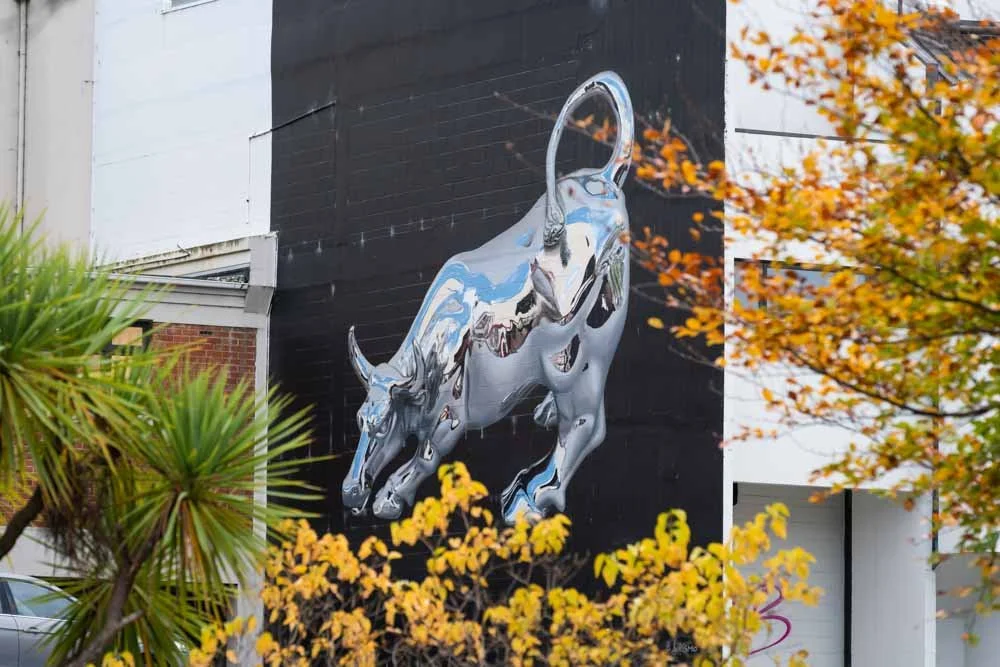 Large mural of a silver bulldog on a black background wall, with trees and autumn leaves in the foreground.