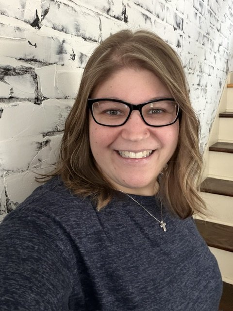 Lady with glasses smiling standing by wall with stairs