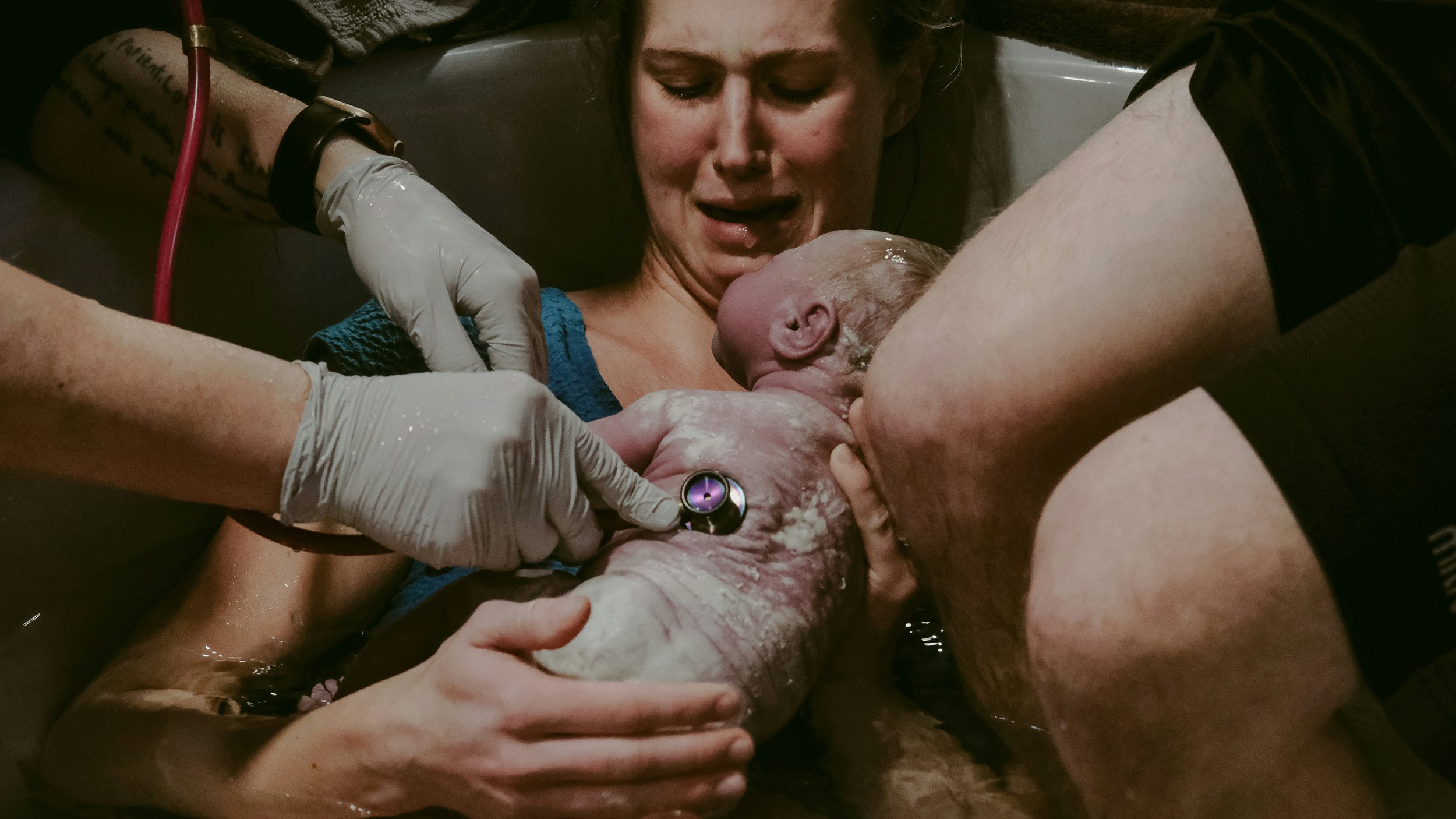 A woman giving birth in a hospital bed surrounded by medical staff assisting with the delivery of a newborn baby.