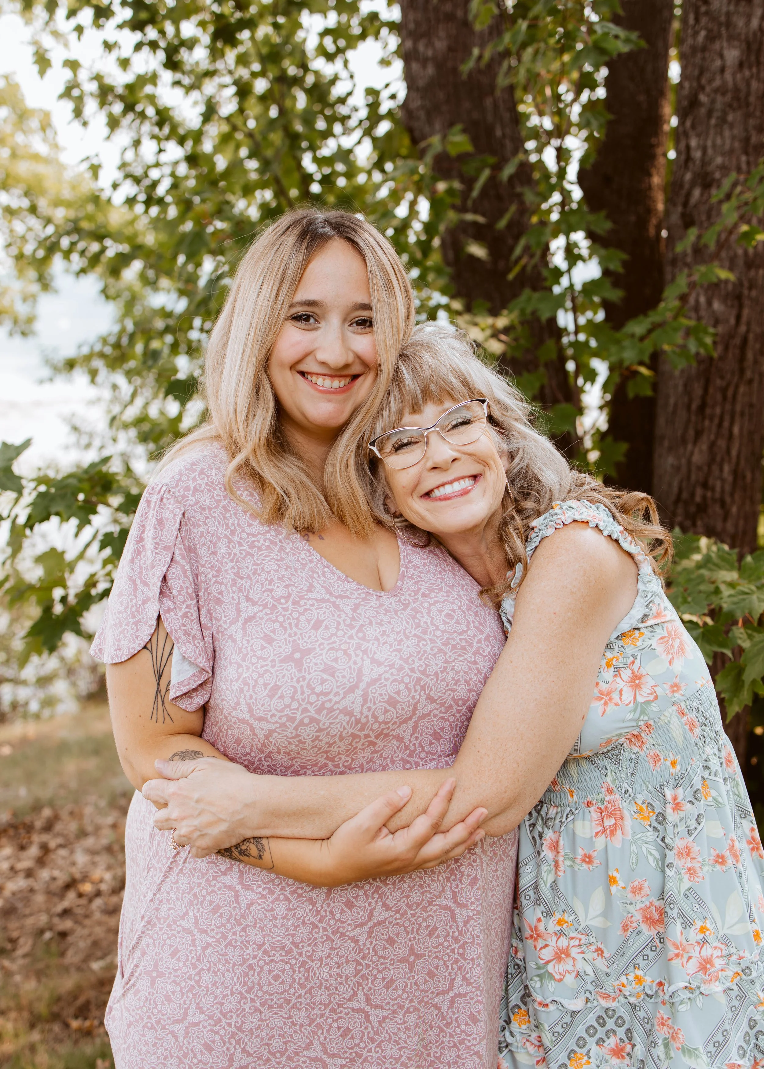 Two Women Outside Hugging By Tree While Smiling