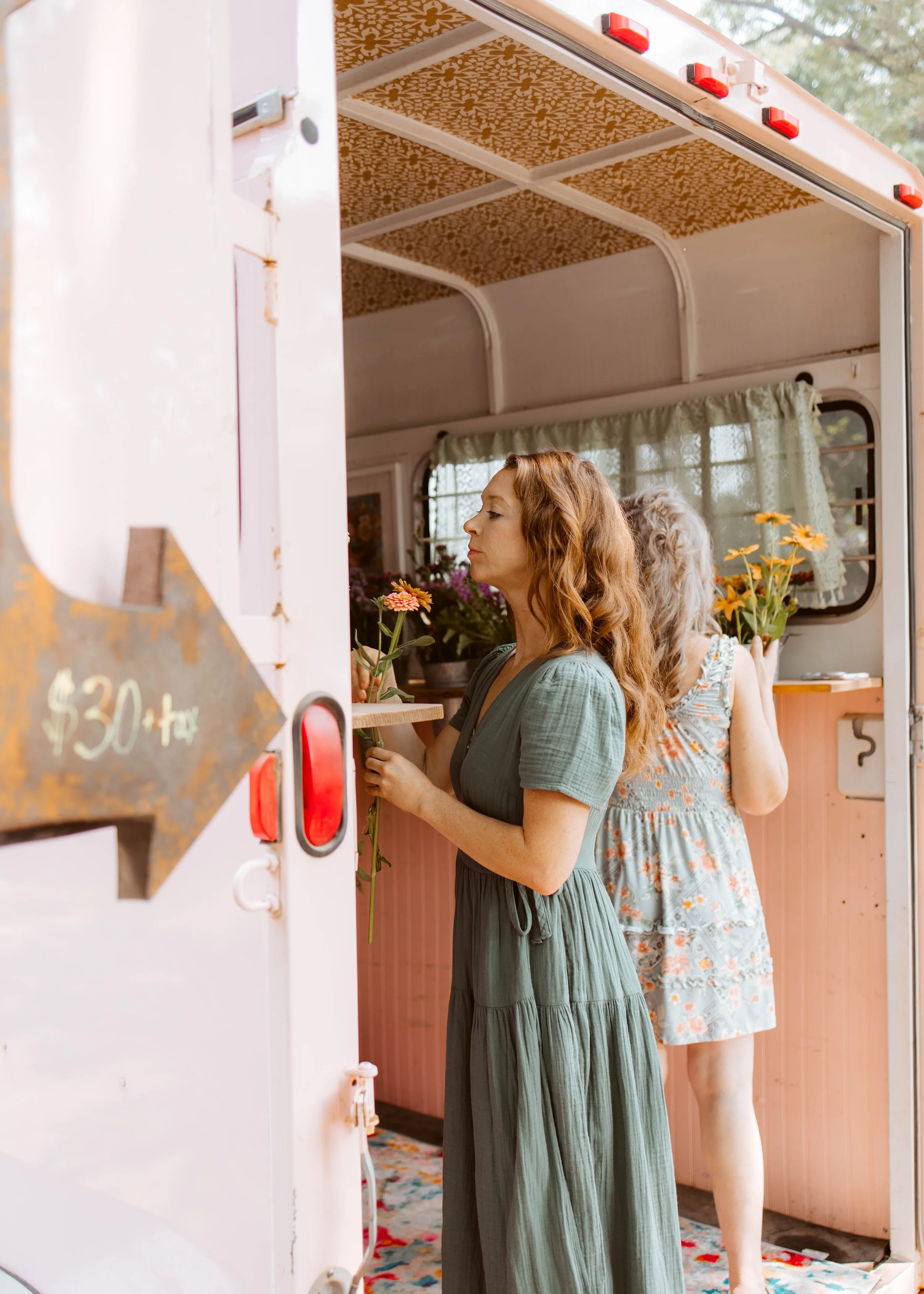 Two ladies in dresses smelling flowers in trailer