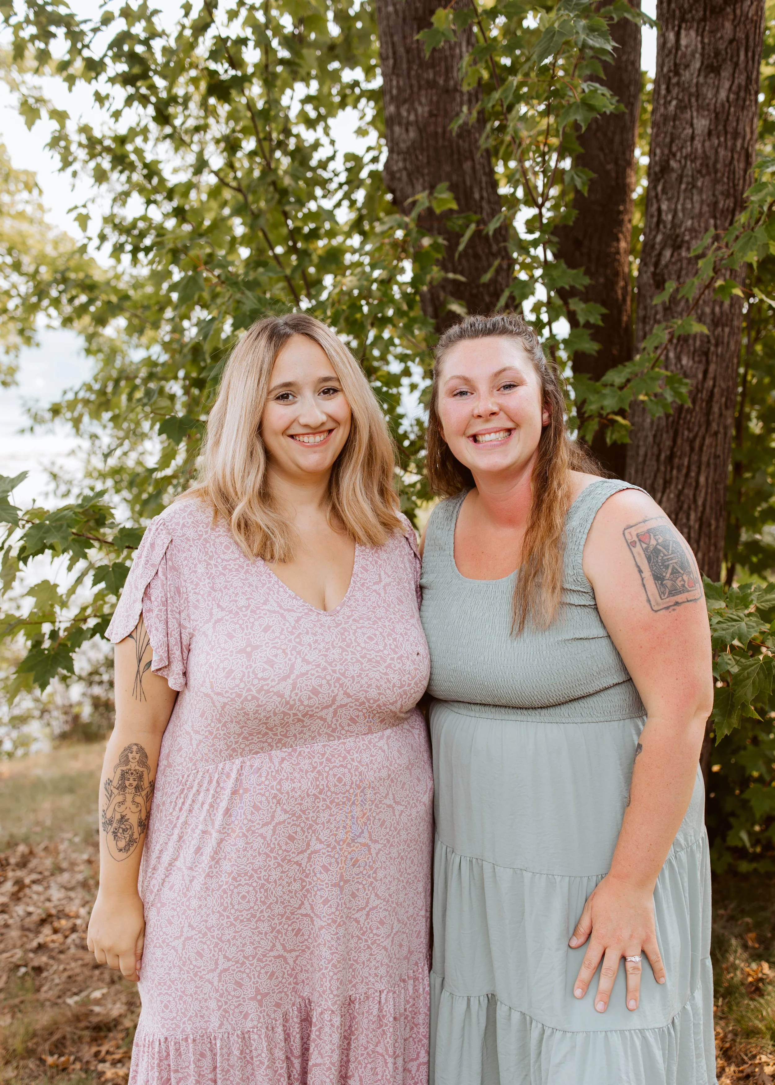 Two Women In Dresses Outside By Tree Smiling