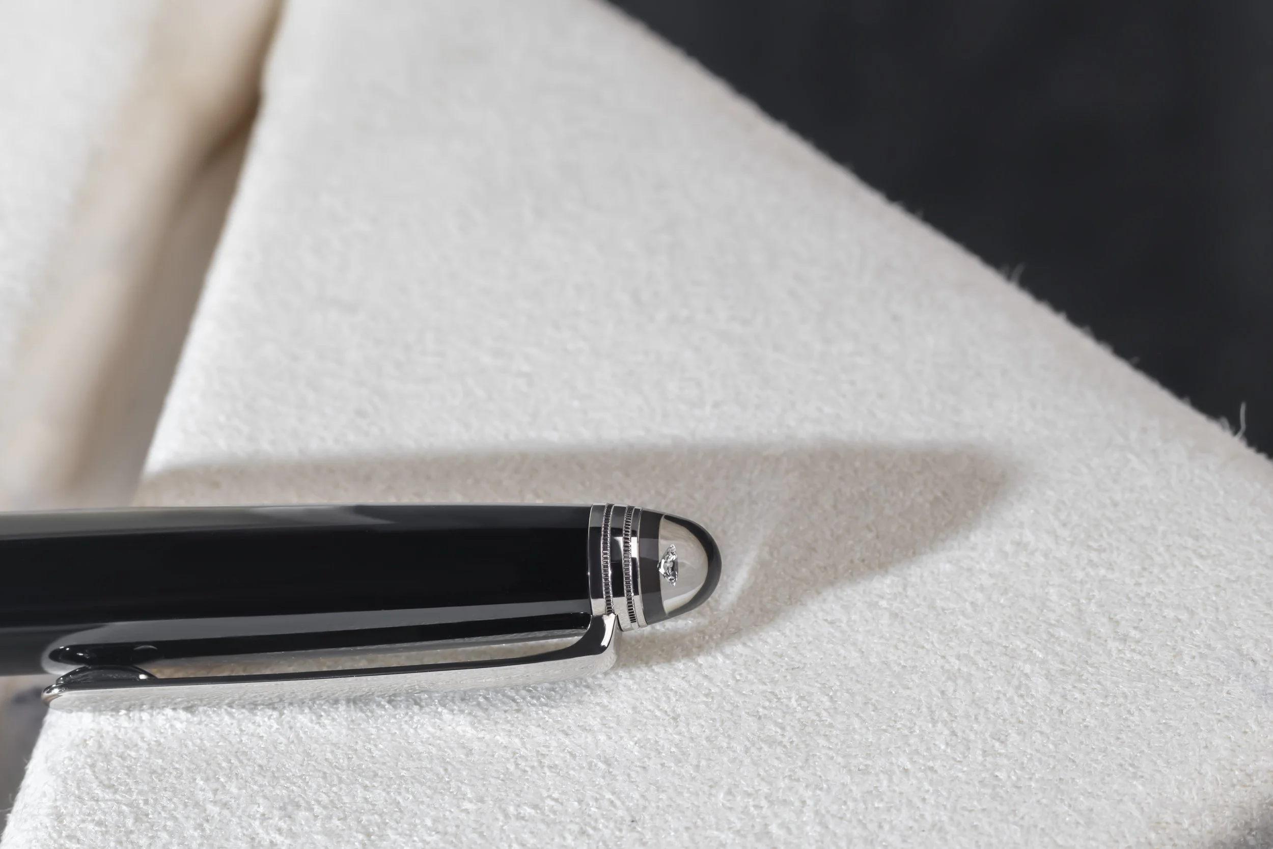 Black and silver pen with a decorative top resting on a white textured surface.