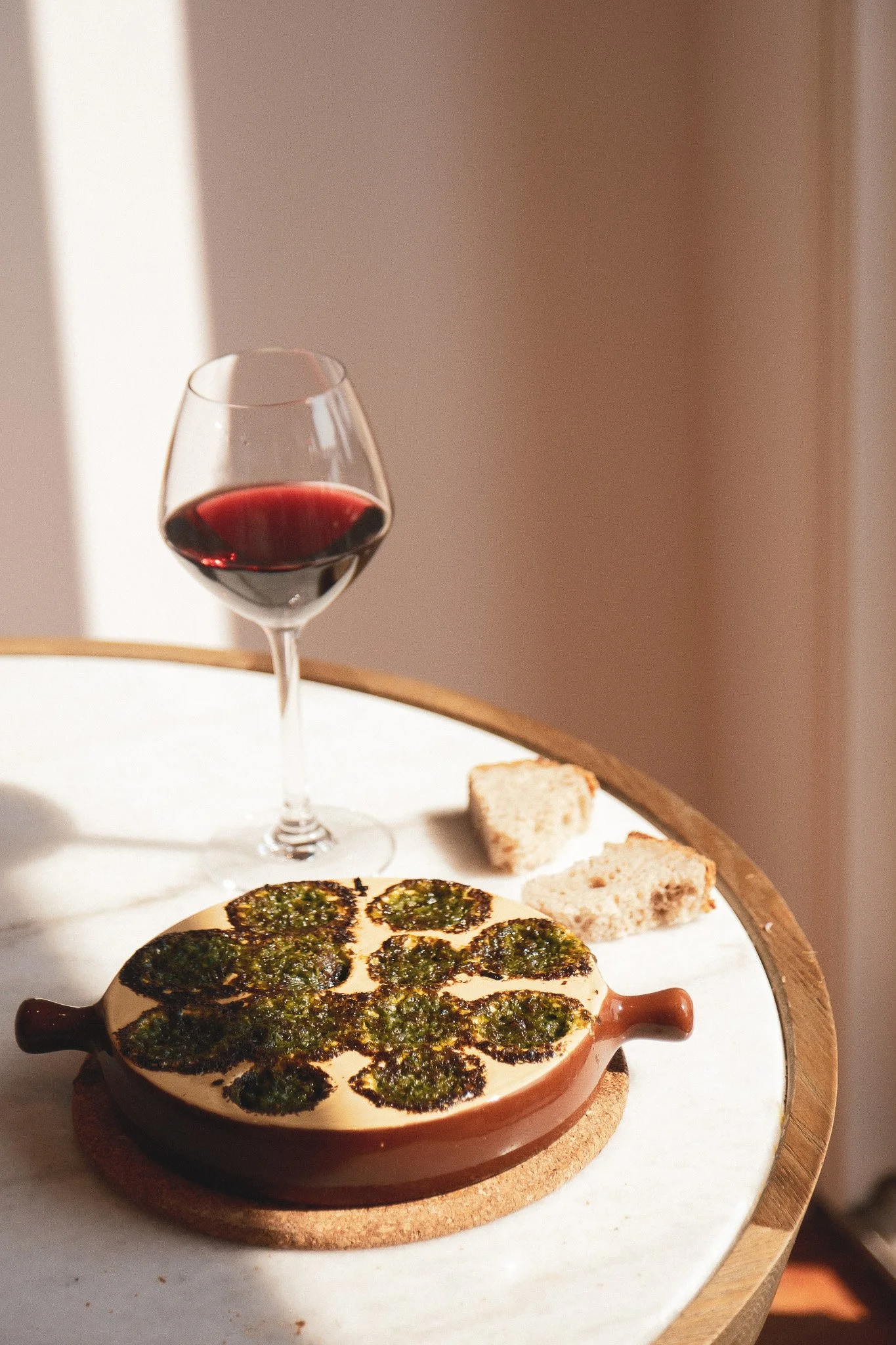 Un plat de fromage recouvert de pesto, avec du pain et une coupe de vin rouge à côté.