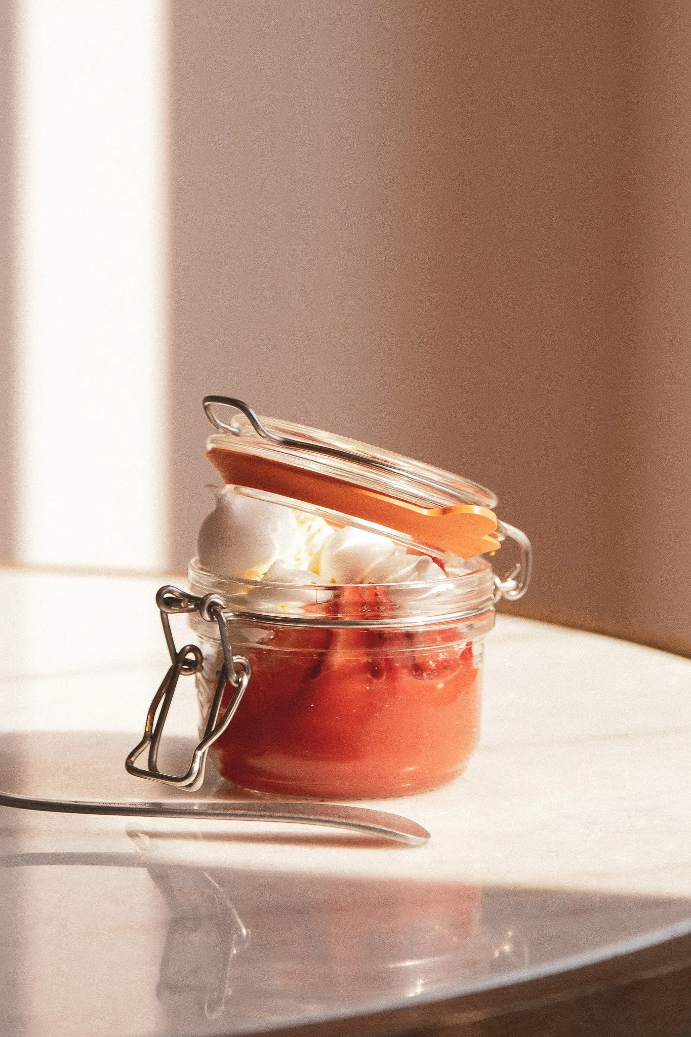 Pot en verre avec une couche de fruits rouges et de la crème, fermé par un couvercle en verre avec une pince en métal.