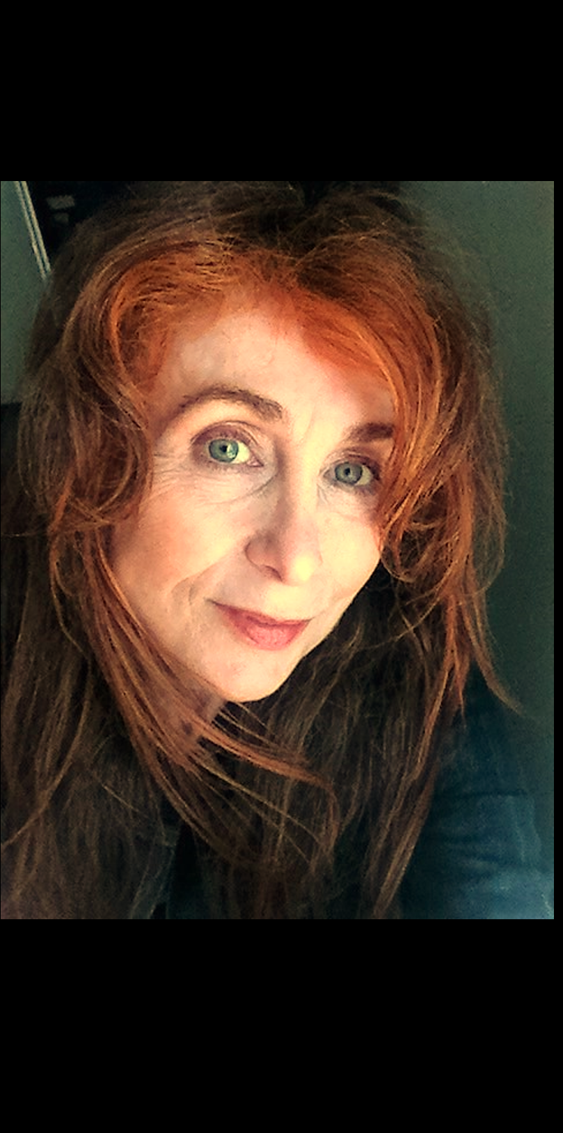 Close-up of a woman with long, wavy red hair and green eyes, smiling slightly at the camera.