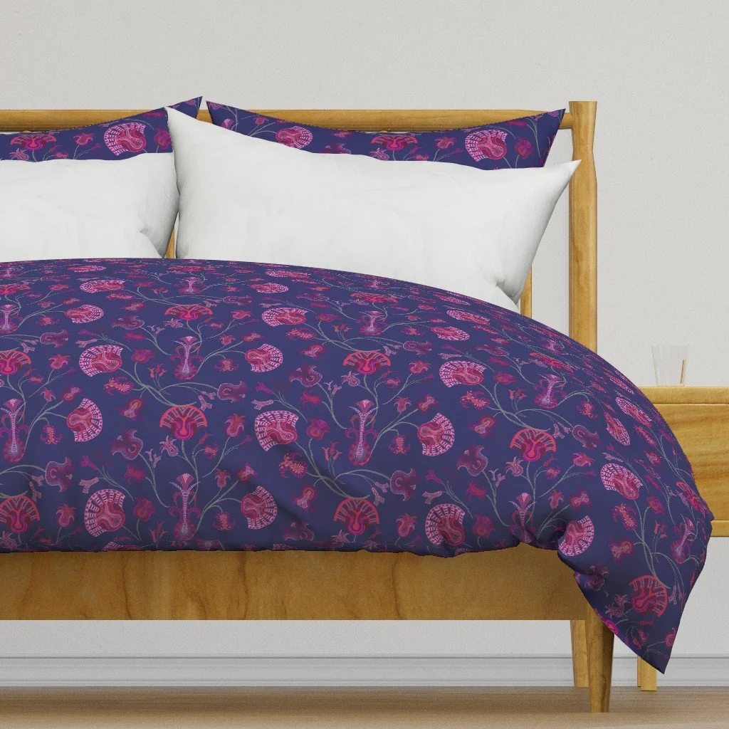 Deep blue wallpaper with glowing pink branching tulip-inspired bouquets on a duvet atop a modern, simple wood-framed bed in a contemporary white room