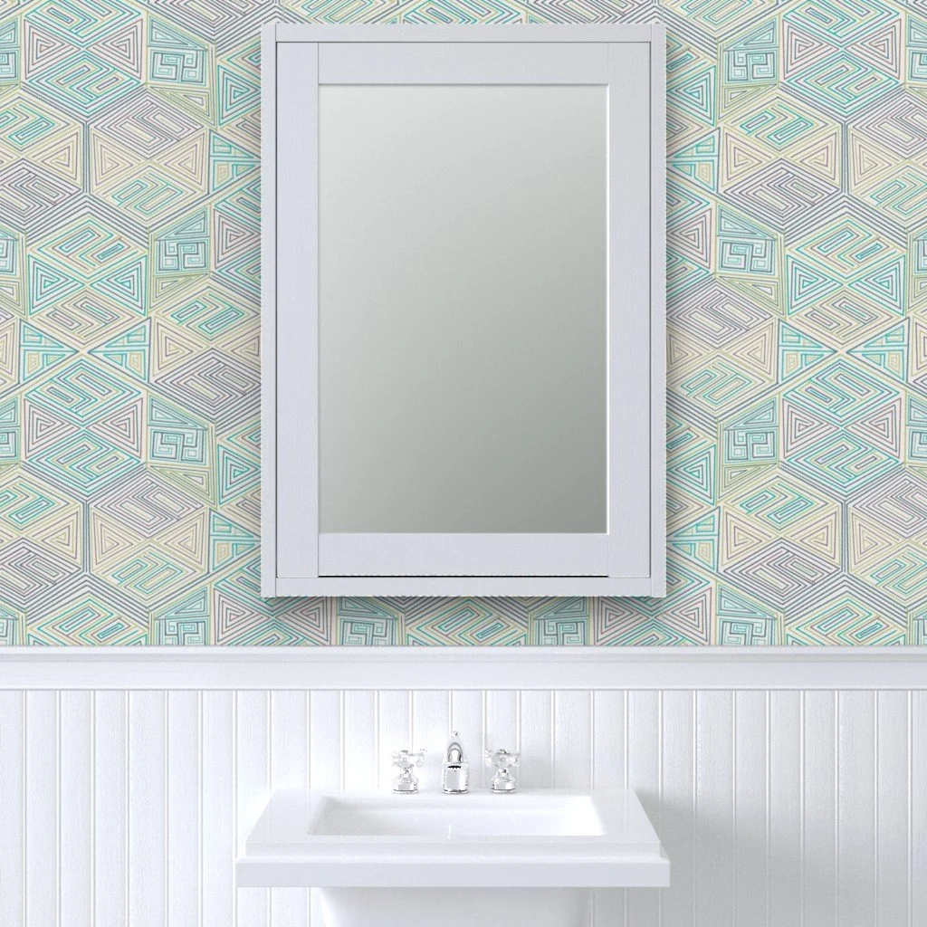 Hand-drawn hexagon geometric wallpaper in seafoam, teal, and grey, shown in a bathroom setting behind a framed mirror. Nested triangle line work repeats across a soft cream ground.