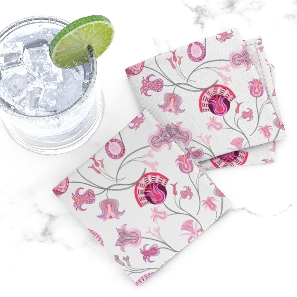 White napkins showing branching tulip-inspired bouquets are folded on a white marble counter next to a glass of club soda with ice and lime