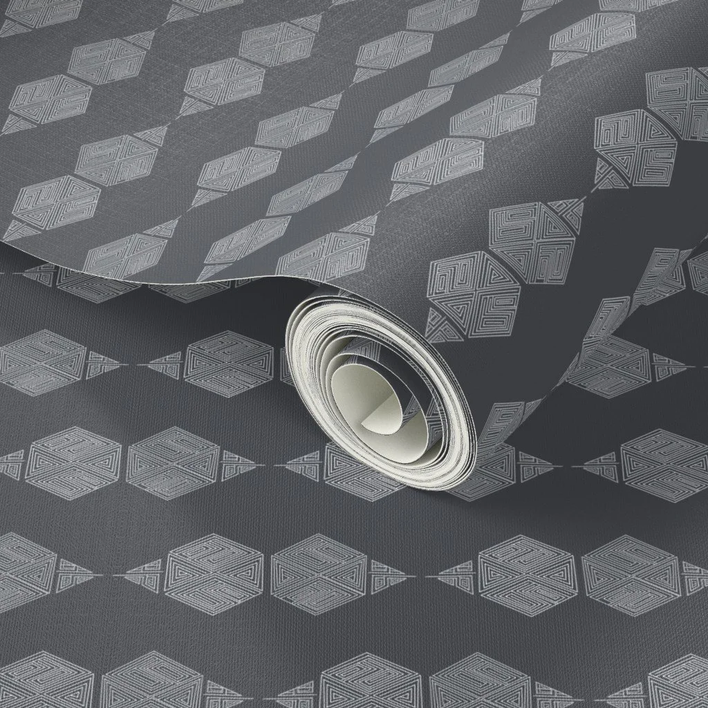 A close-up of the charcoal grey geometric wallpaper, showing the hand-drawn hexagon motif at small scale with its flanking triangular points. Pale grey maze-like line work stands out against the dark charcoal ground