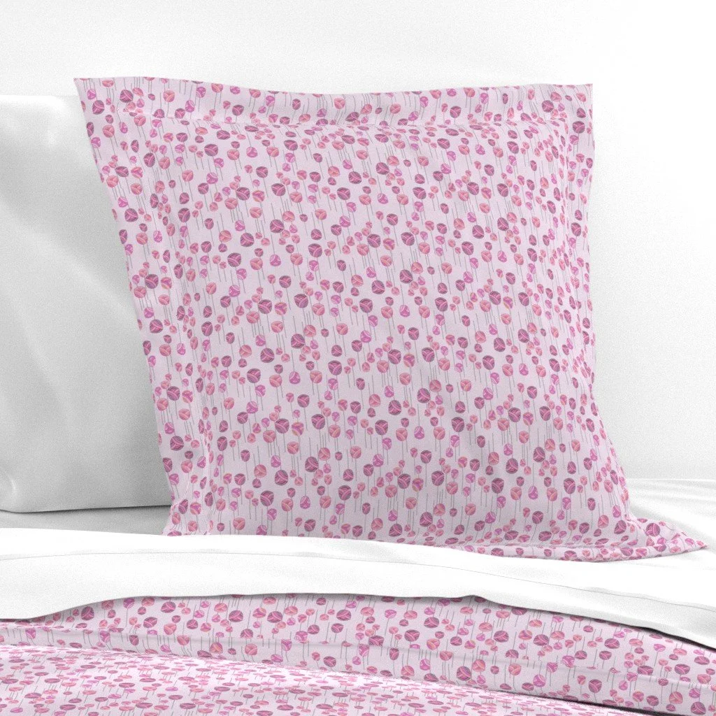 A dancing floral ditsy pattern with abstract tulips and stems on a light pink background on a pillow leaning against a white wall and crisp white sheets