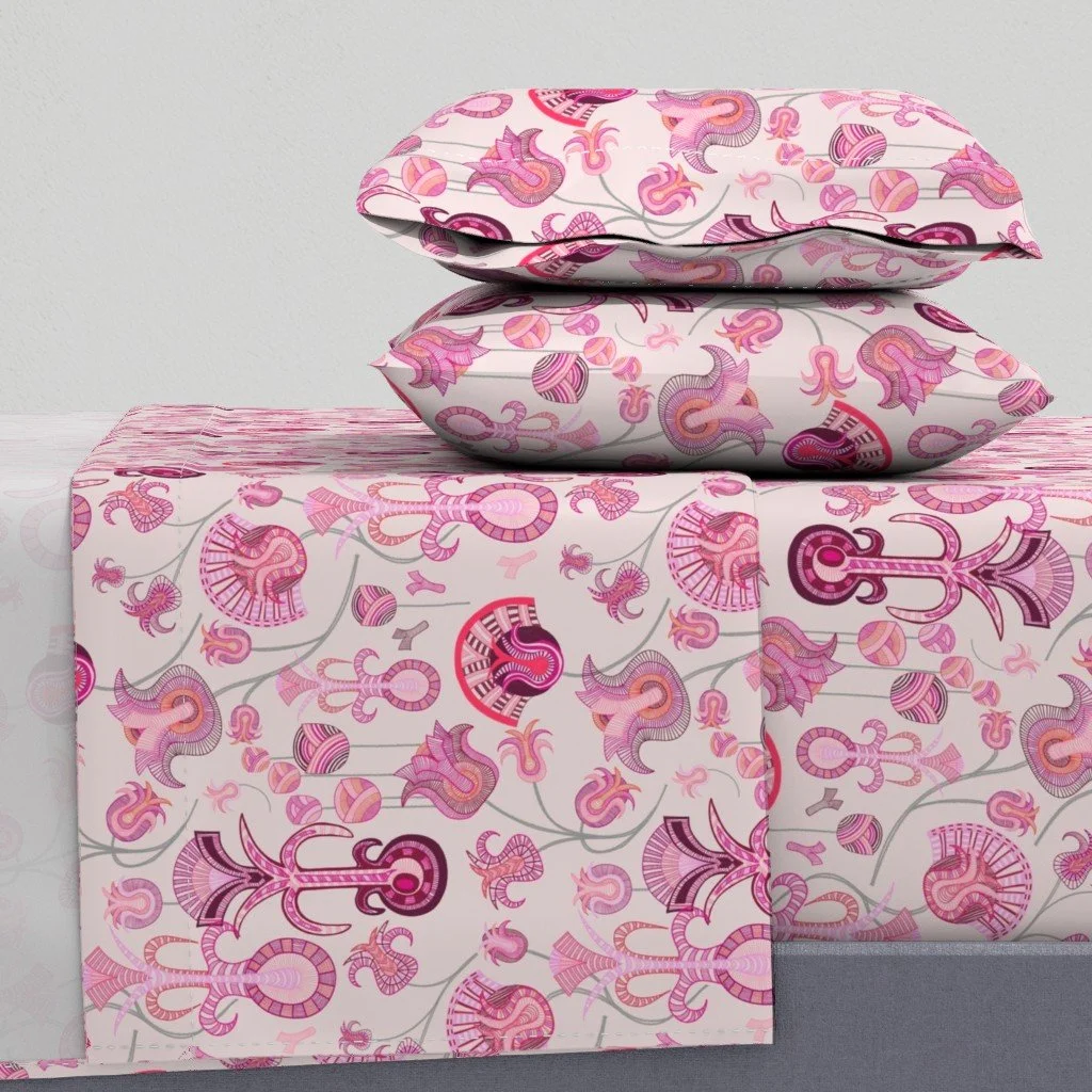 Layered tulip-like forms with intricate detail play across a warm pale ground upon a sheet set and pillows stacked on a bed