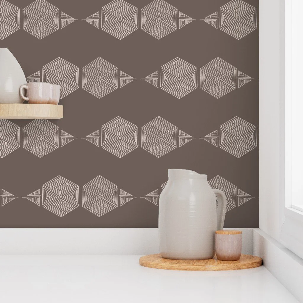 A brown and taupe hand-drawn hexagon wallpaper behind a pristine white counter top with a shelf on the left holding glassware and a pitcher and cup in the corner on the counter up against a window
