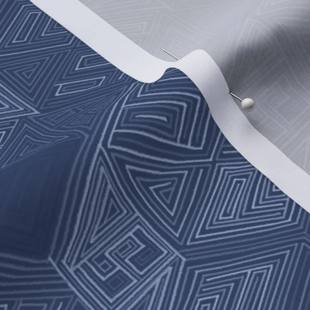 A close-up of hand-drawn hexagon geometric fabric in monochrome navy, pinned at the fold to show drape and weave. Pale blue maze-like line work traces across a deep indigo ground.