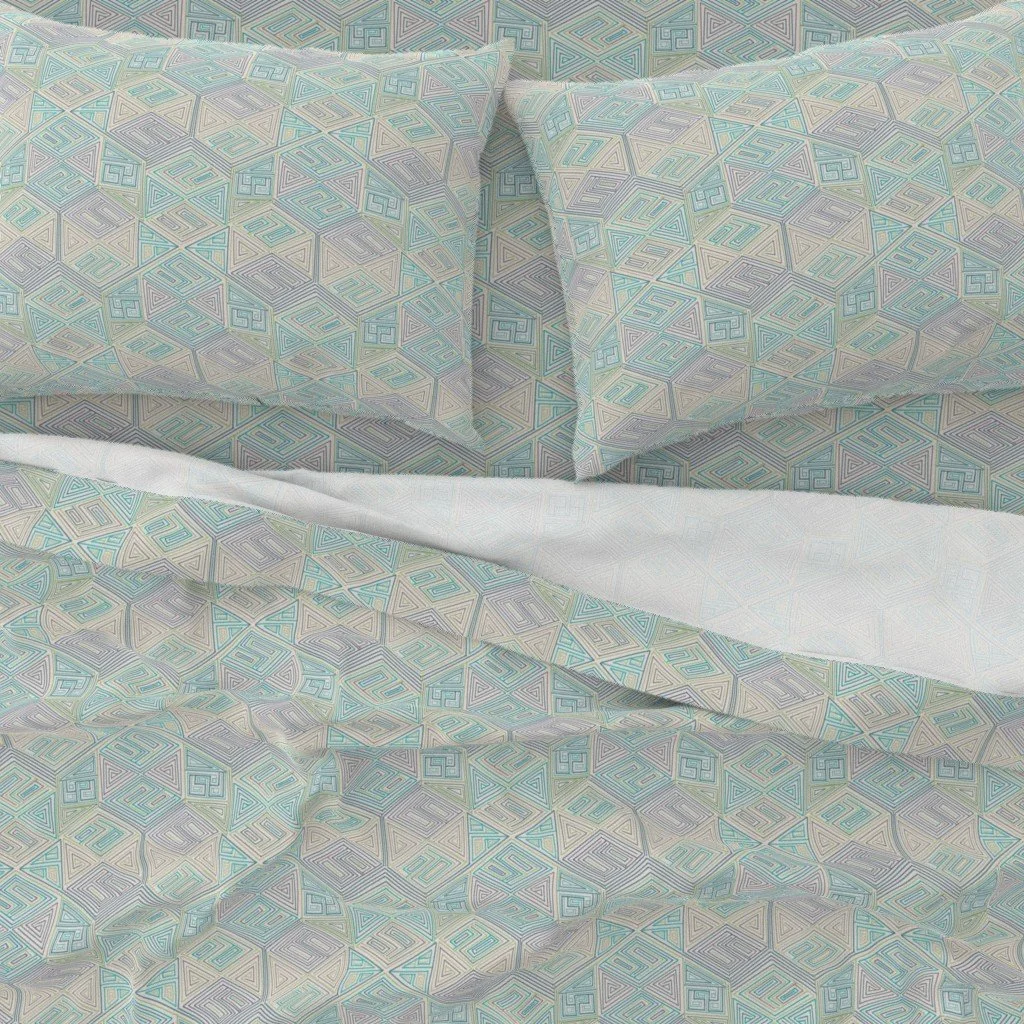 A close-up of hand-drawn hexagon patterned bedding in cool seafoam, teal, and warm grey. Maze-like nested lines repeat across a duvet and pillow shams, with sheet shown folded back at the top.