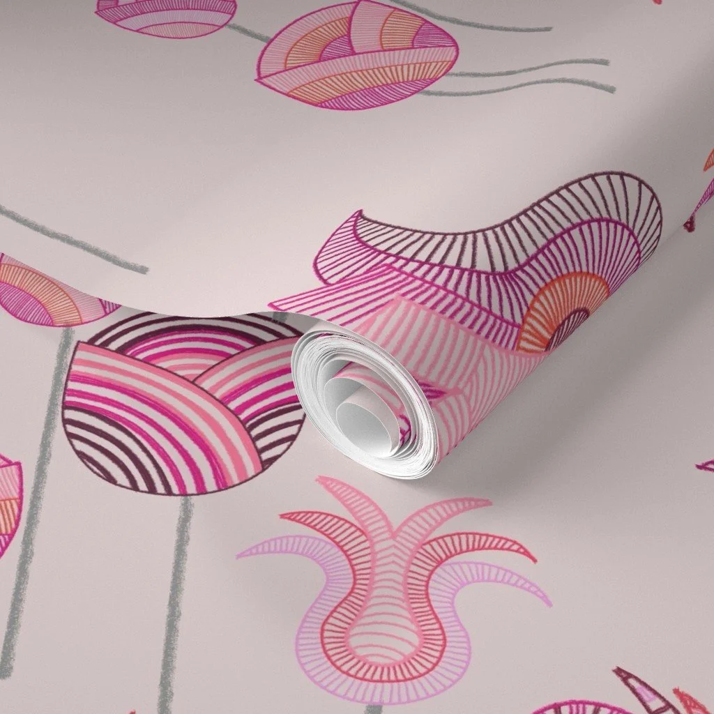 Whimsical tulips meander and sprout with detailed vibrancy against a light pink shown on a roll of wallpaper 