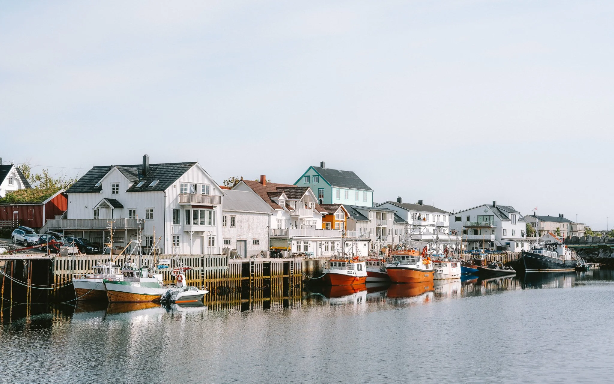 Colorful boats docked along a marina with white houses with different colored roofs on the shore.
