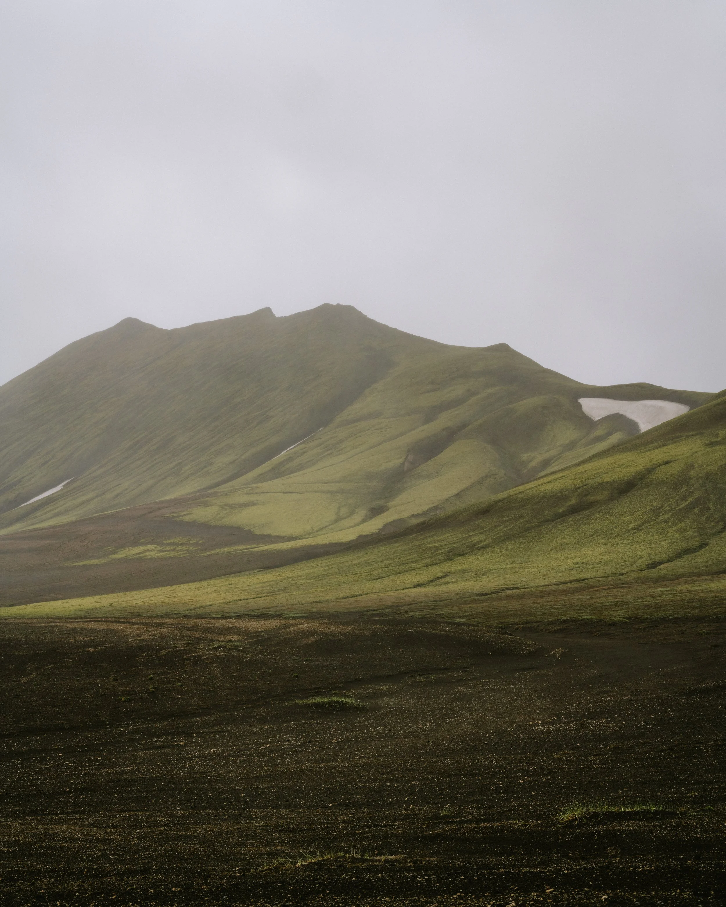 A green, moss-covered mountain with a cloudy sky in the background.