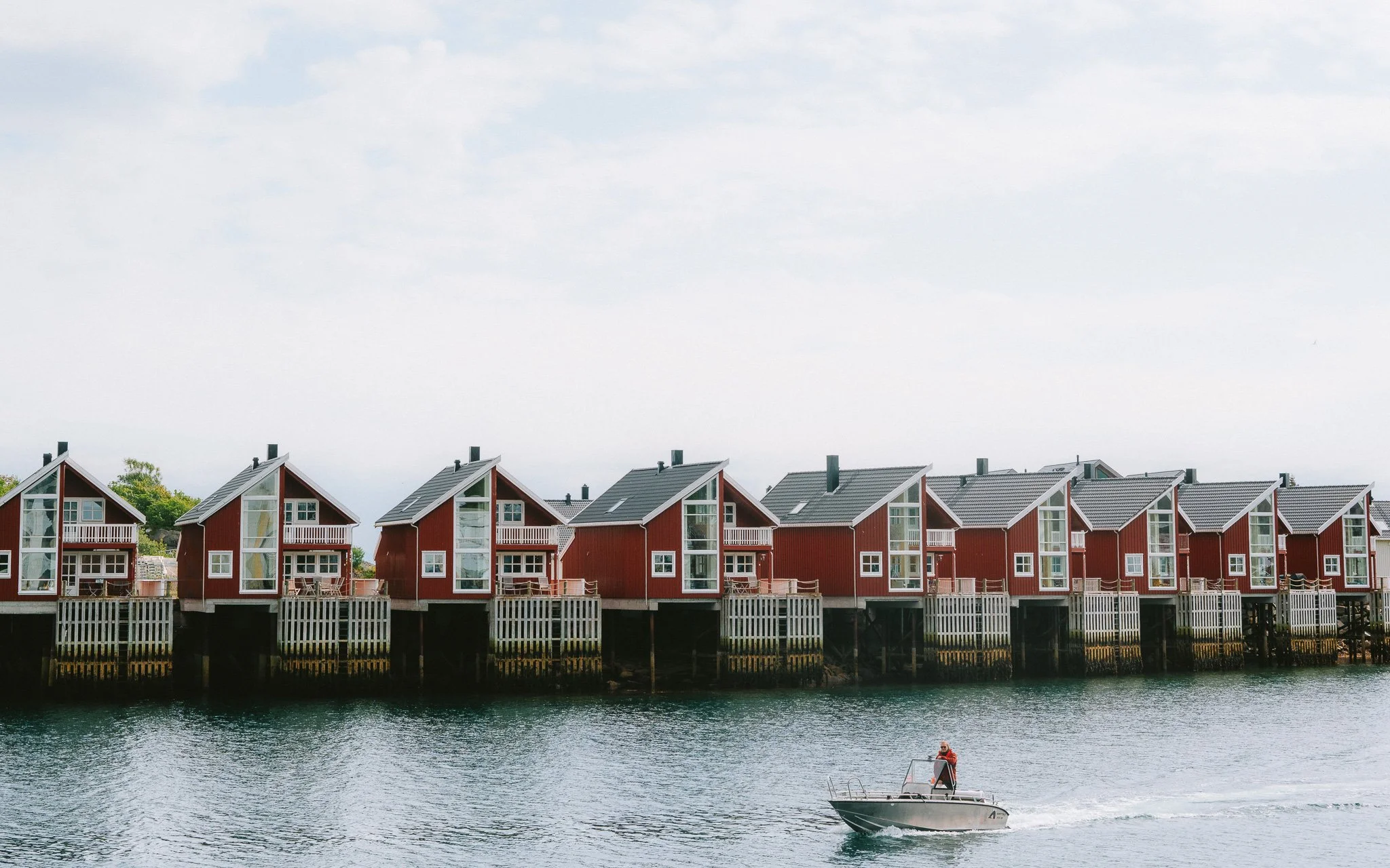 A row of red houses on stilts along a waterfront, with a person in a small motorboat in the water in front.
