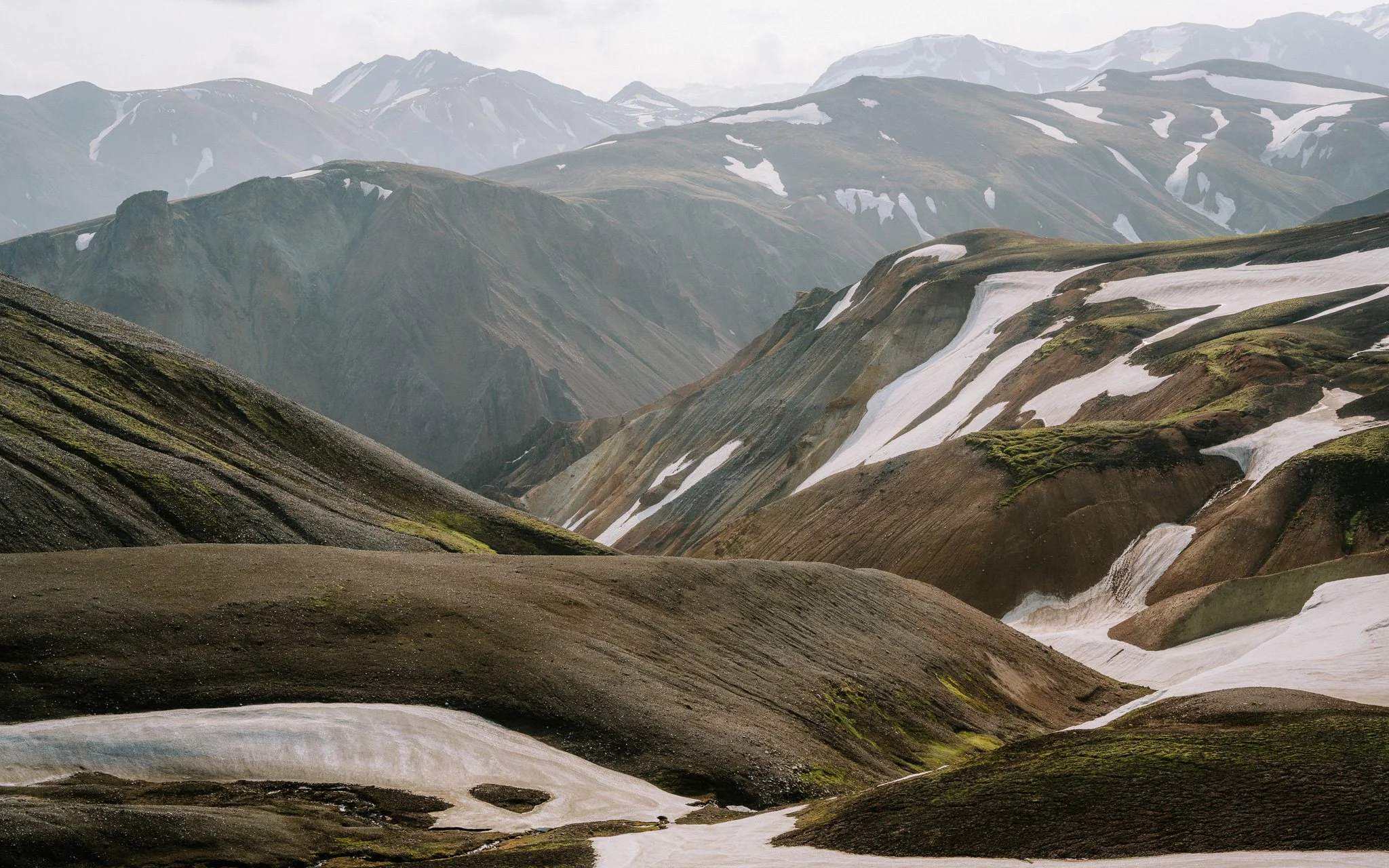 Mountain landscape with rugged hills, snow patches, and green mossy areas.