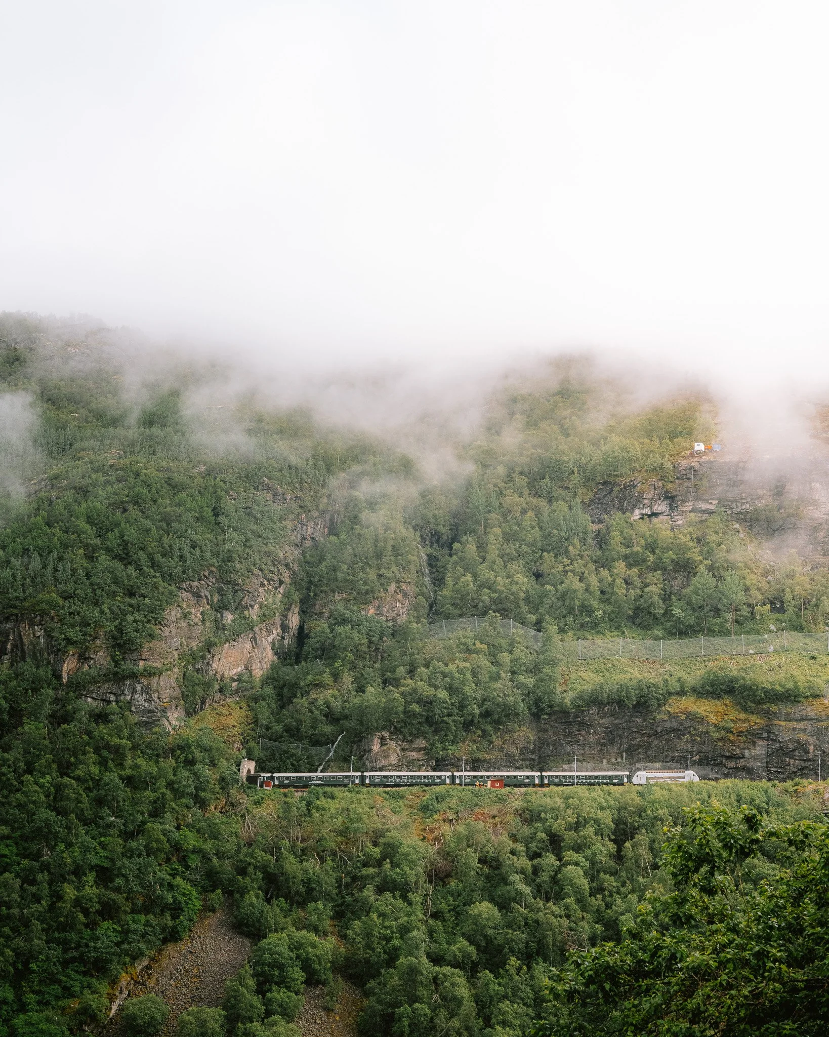 Train traveling through green mountains with fog and mist.