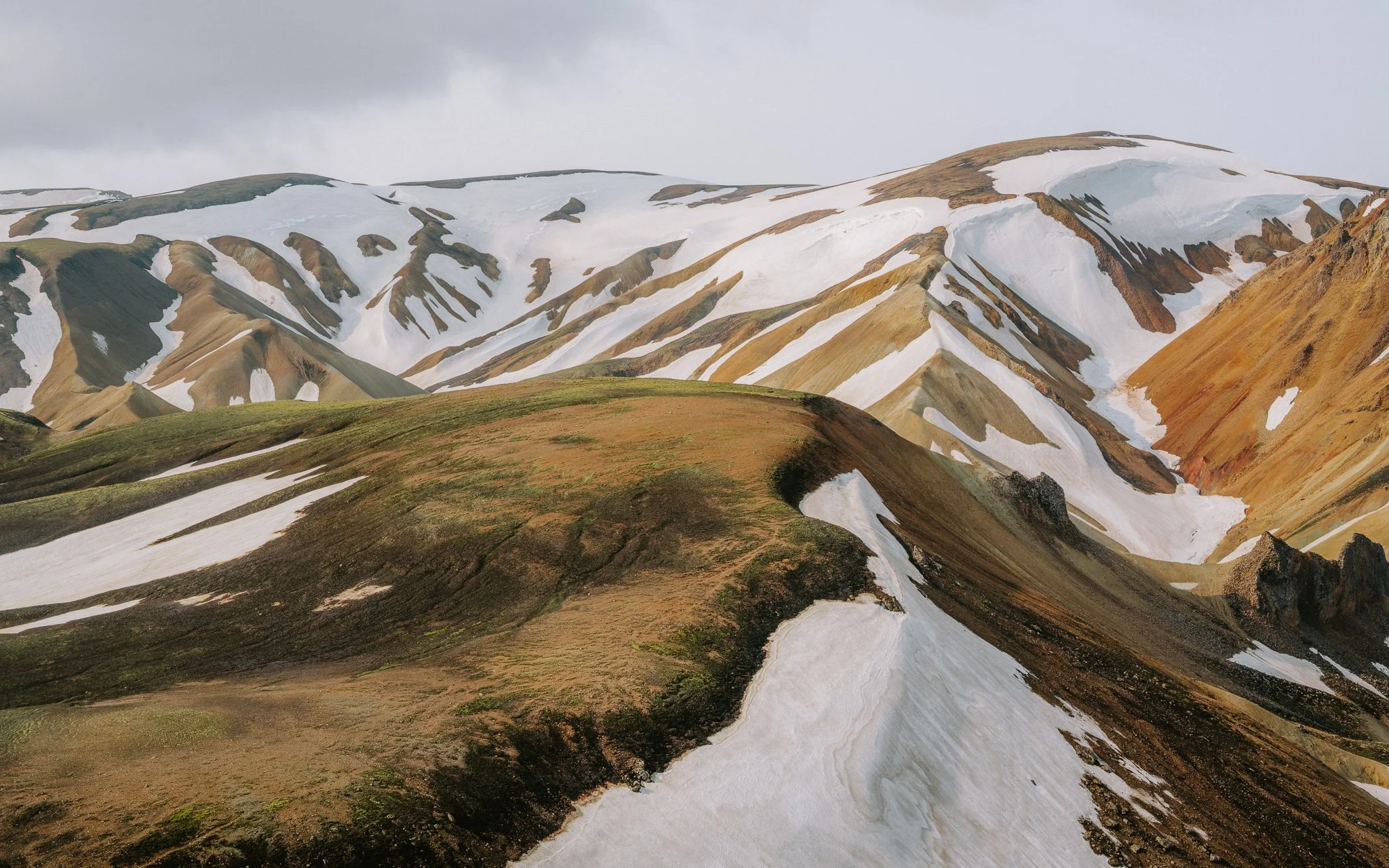 Mountain landscape with colorful ridges, patches of snow, and grassy slopes.