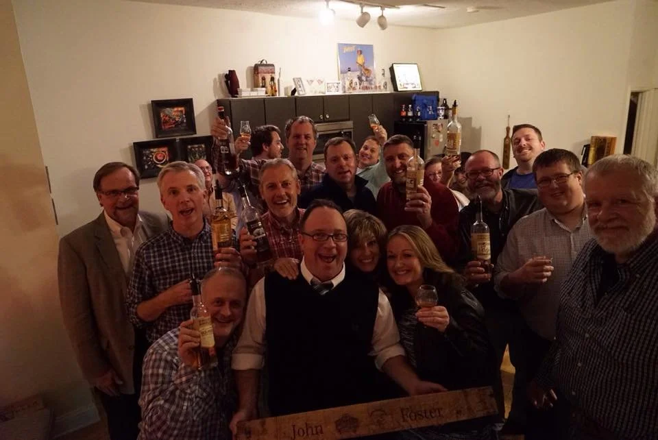 Group of people celebrating with drinks in a living room, smiling and raising glasses.