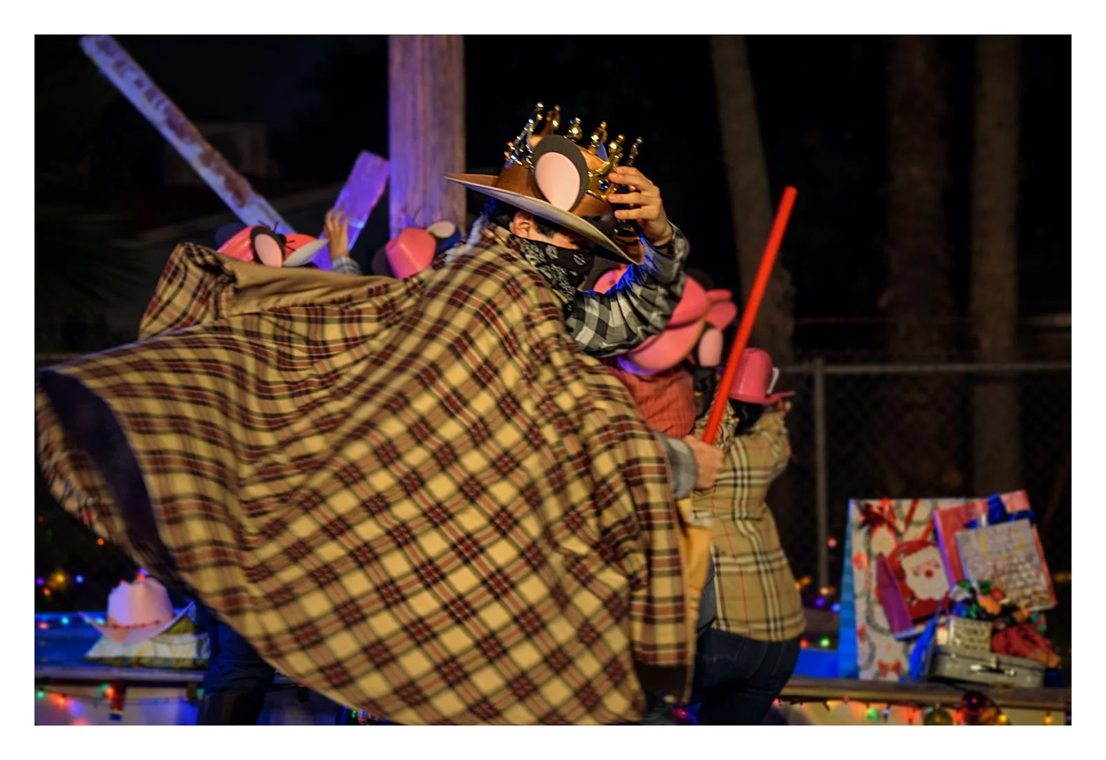 Personas con disfraces de Navidad bailando durante una fiesta al aire libre con decoraciones y regalos navideños.